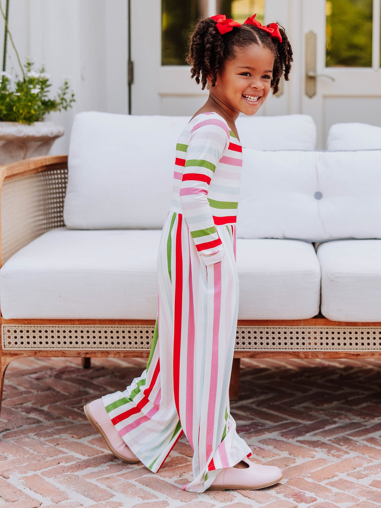 Model standing in front of white couch wearing a multi striped leggy romper. 