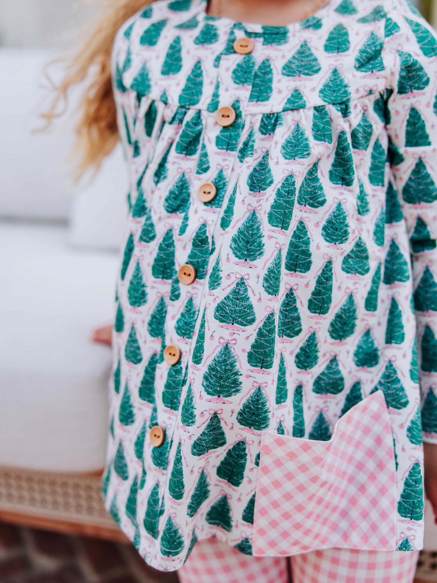 Close up of buttons on Christmas tree themed top with pink gingham pockets. 