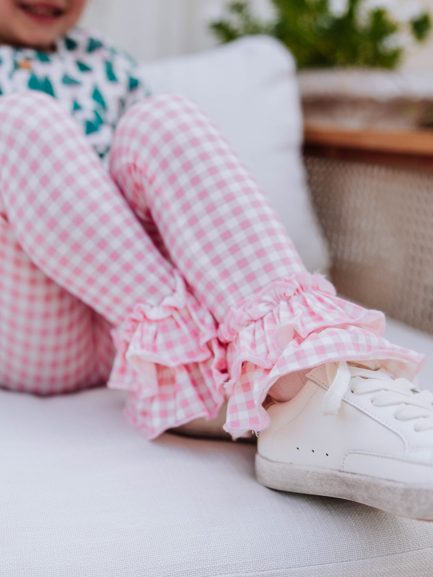 Girl has ankles crossed to show the ruffles at bottom of ankles. Leggings are pink gingham.