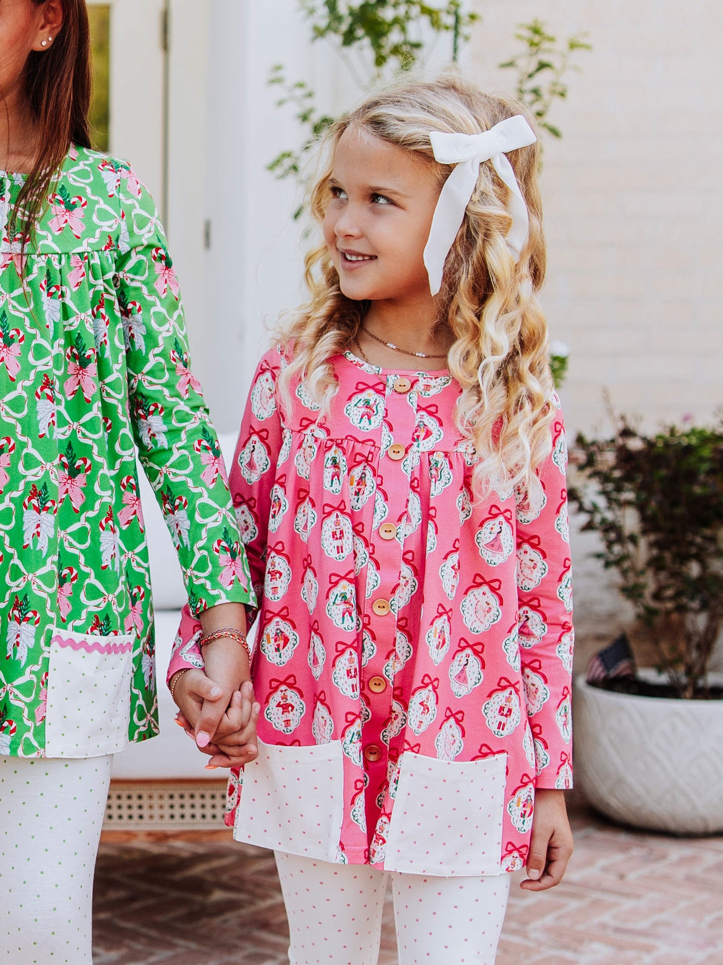 Two girls holding hands both wearing similar style tops with different holiday themed patterns. 