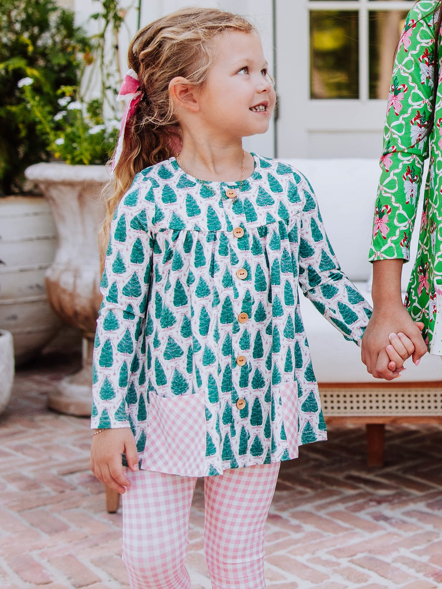 Girl wearing a Christmas tree themed top holding hands with someone else. Girl's bottoms are pink gingham