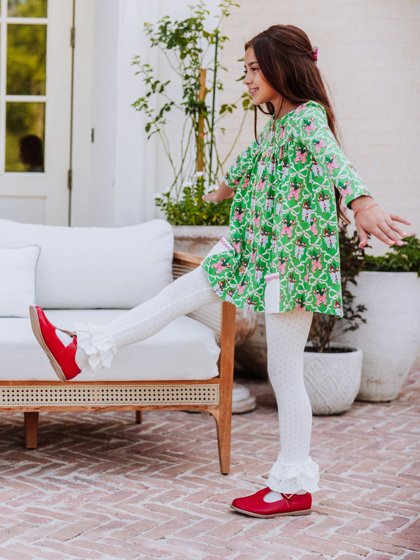 Girl kicking leg out wearing a holiday themed outfit with red mary janes. 