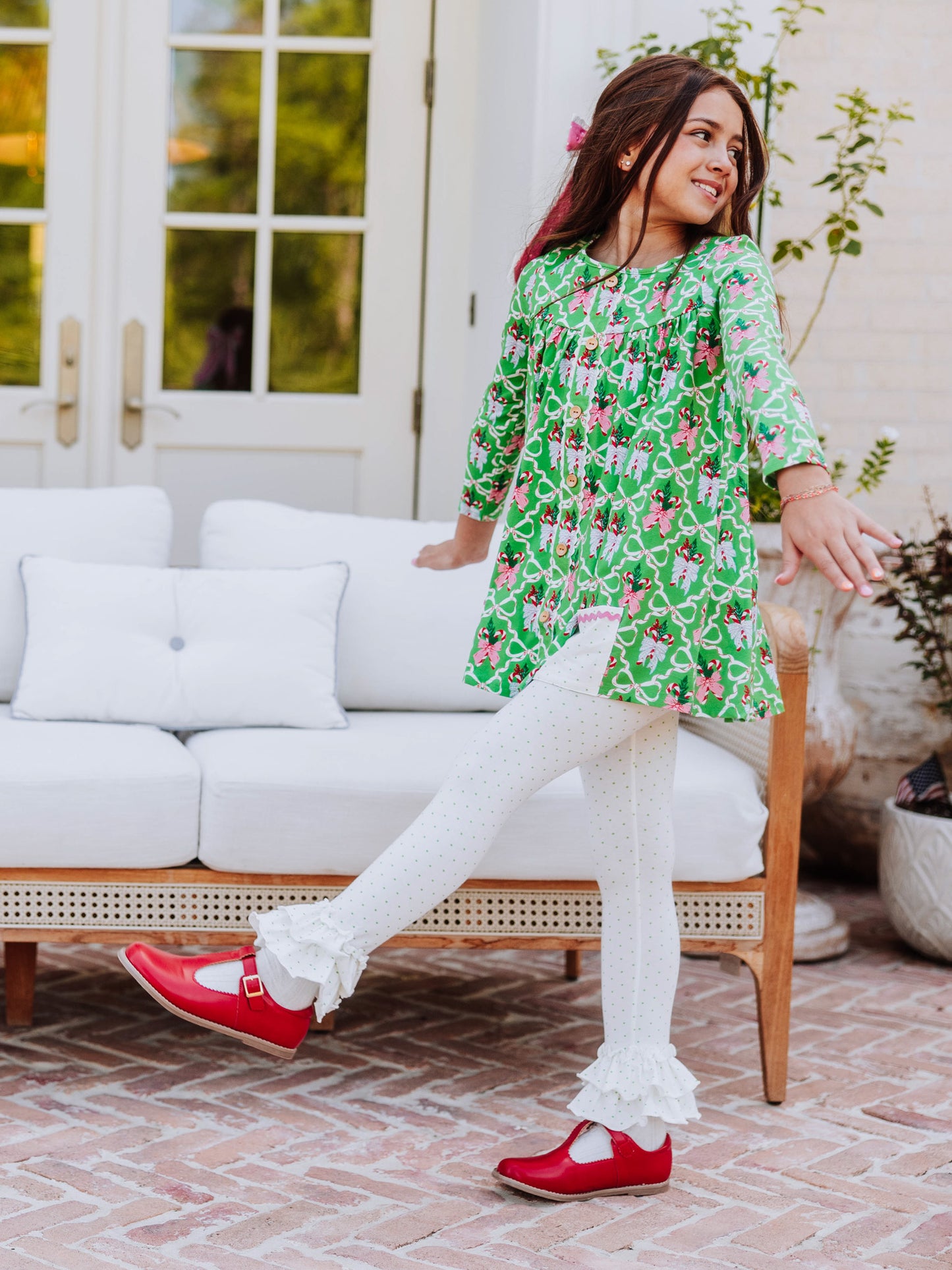 Girl kicking her leg out wearing a holiday themed outfit with red mary janes. 