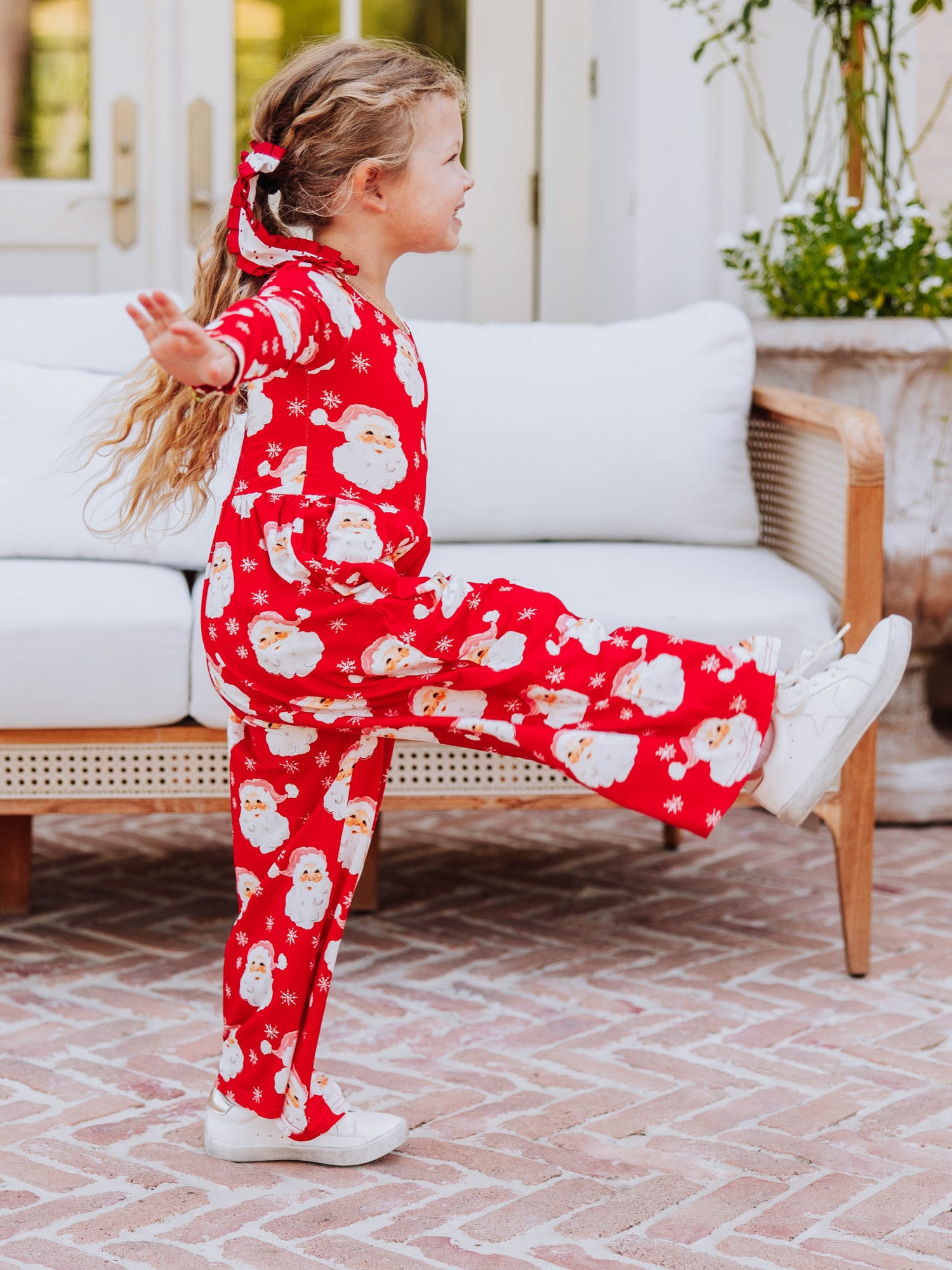 Girl kicking out leg wearing a jolly santa leggy romper. 