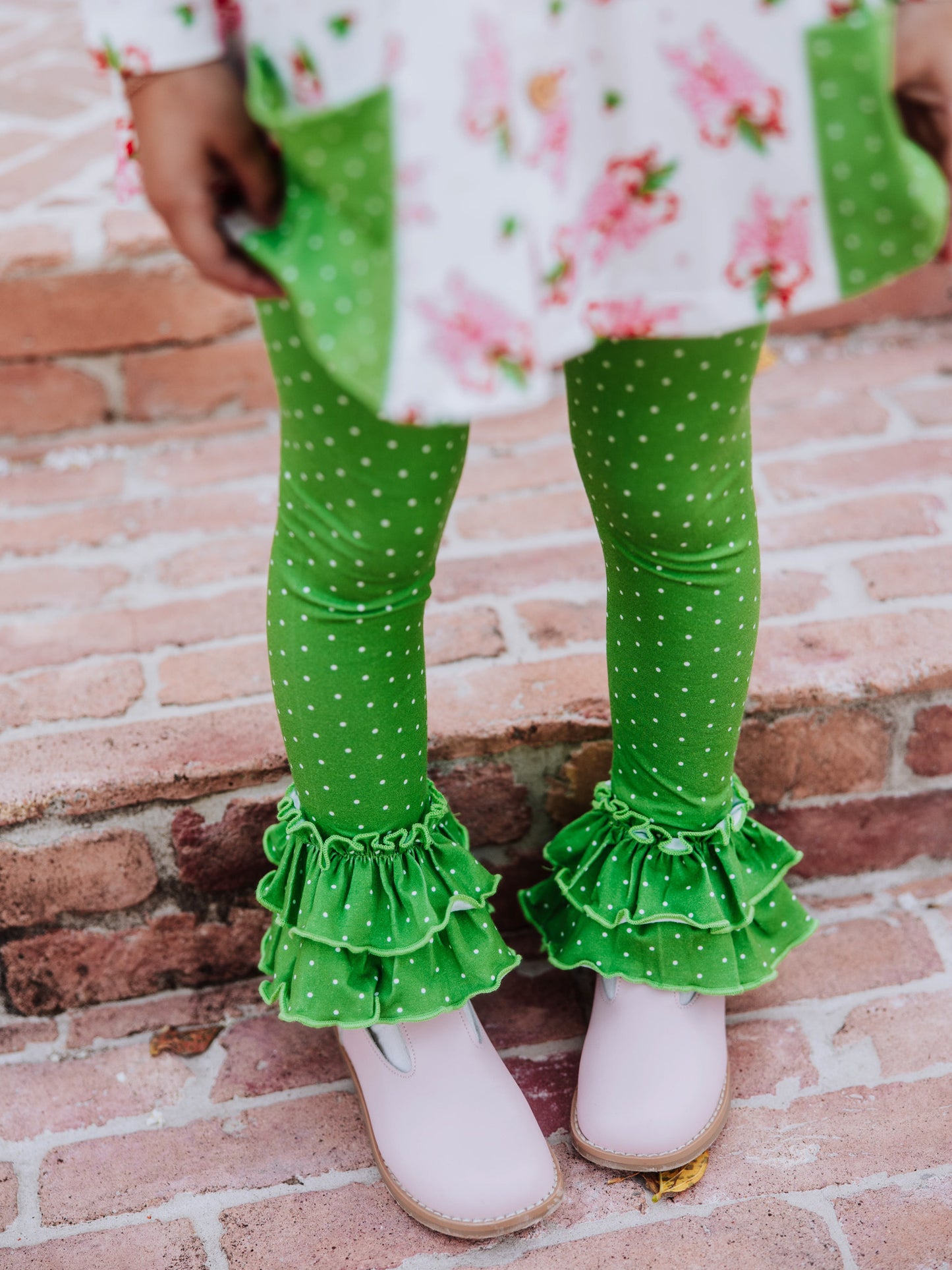 Close up of green leggings with white polka dots and ruffles at bottom. Model is also wearing pink buckle boots. 
