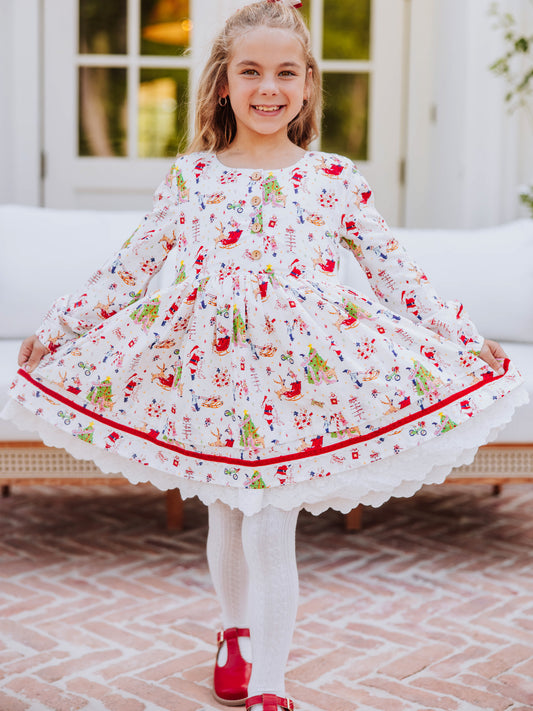 Girl wearing a holiday themed dress and is holding it on both corners to see. Girl also wearing white tights with red mary janes. 