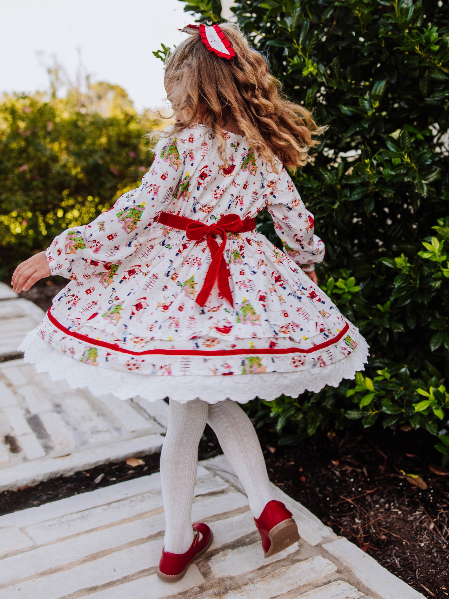 Girl outside twirling in a holiday themed dress. The back of dress has a velvet tie. 