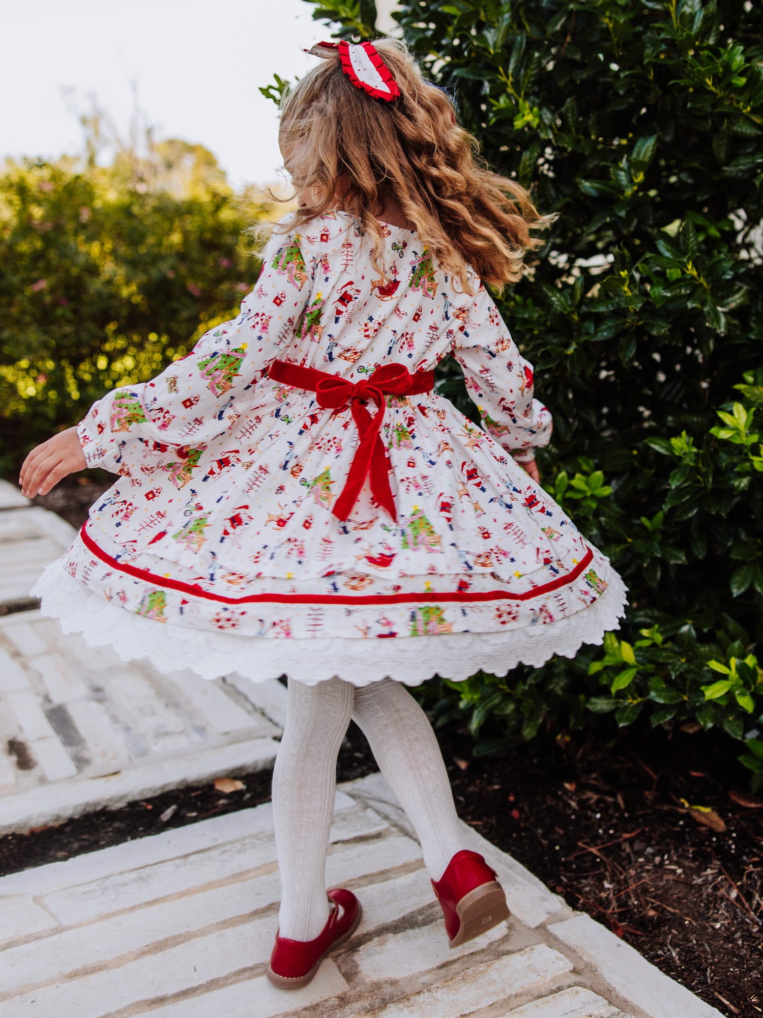 Girl outside twirling in a holiday themed dress. The back of dress has a velvet tie. 