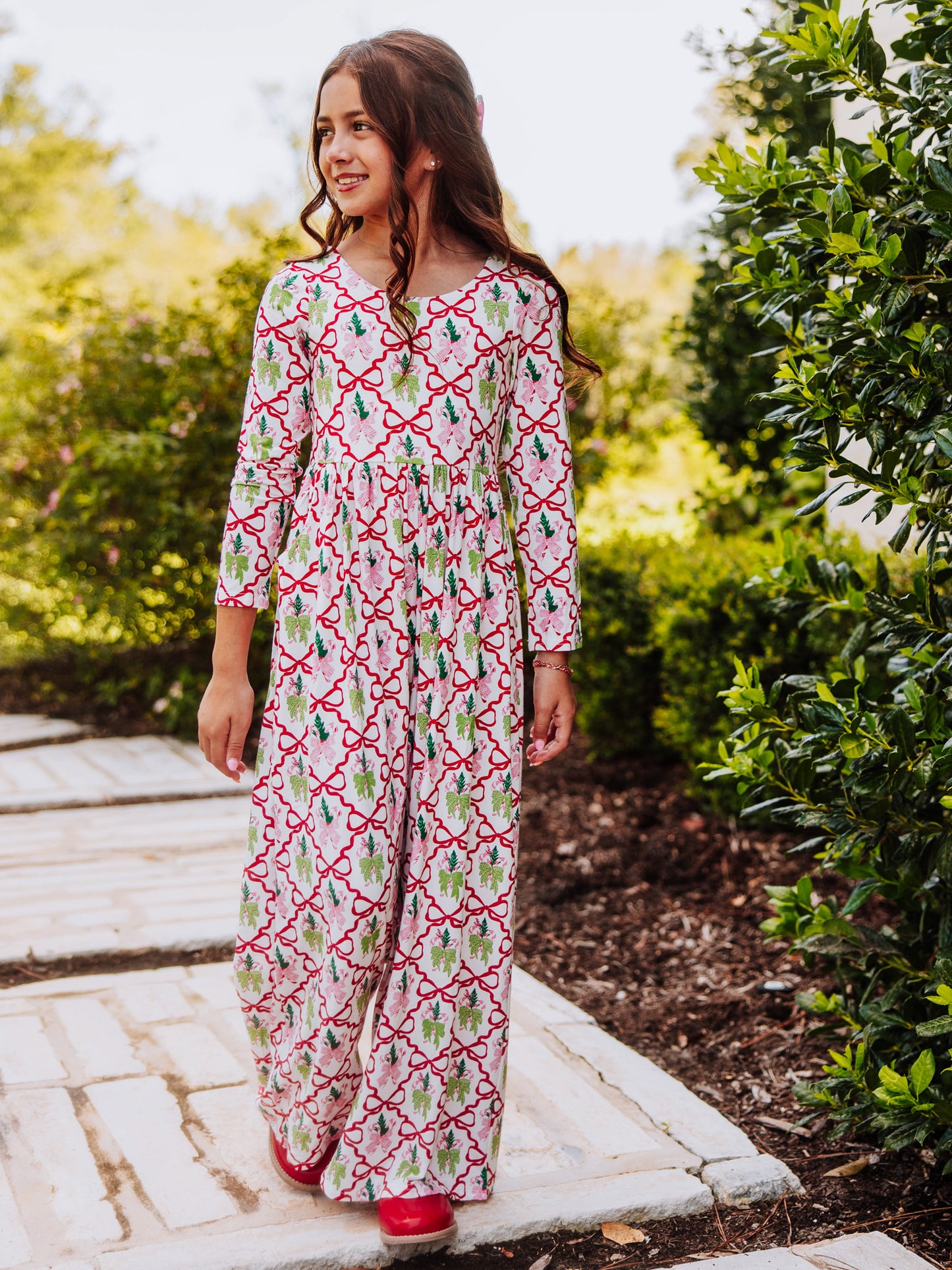 Girl wearing a holiday bow themed leggy romper outside near a bush