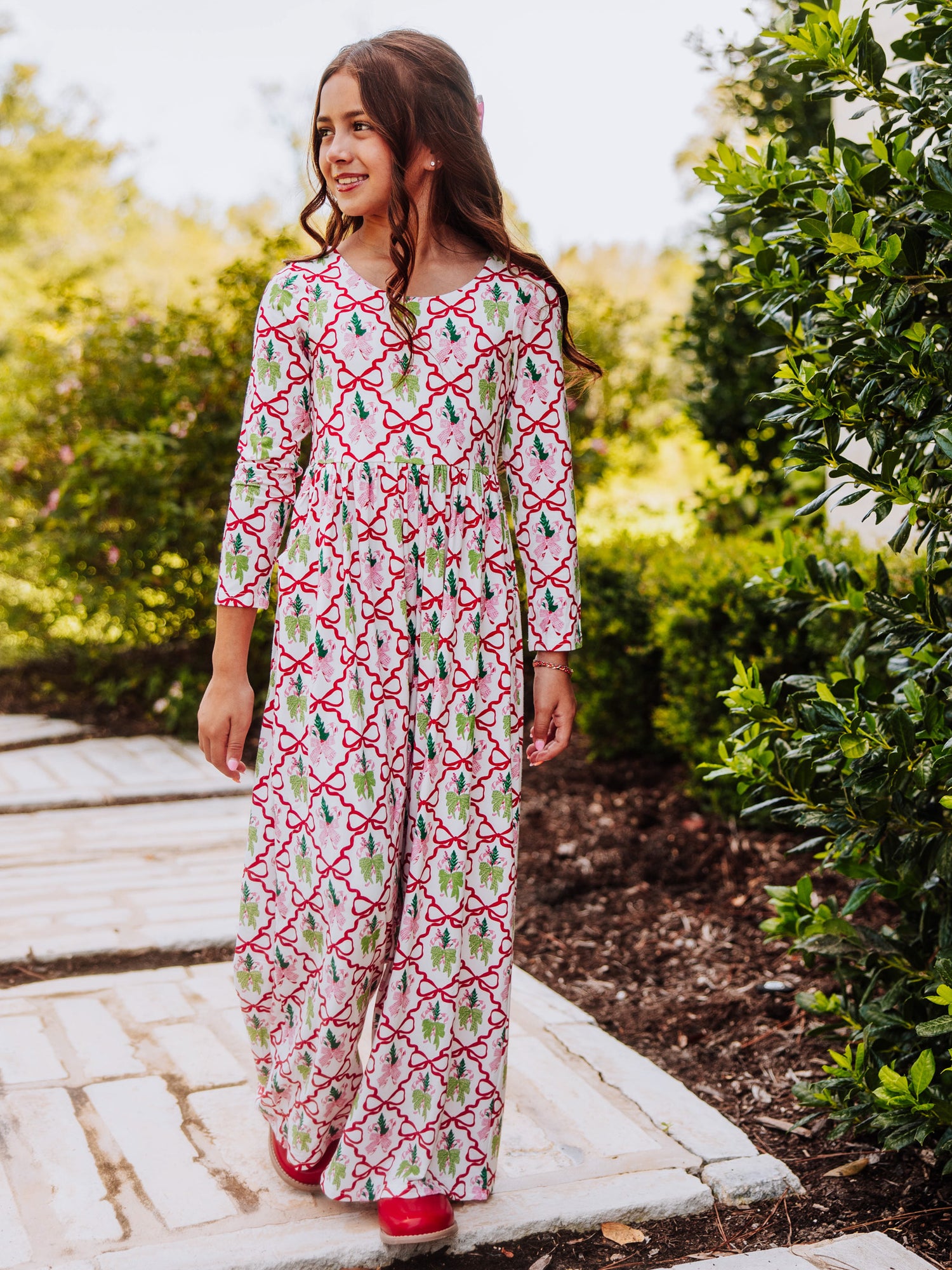 Girl wearing a holiday bow themed leggy romper outside near a bush