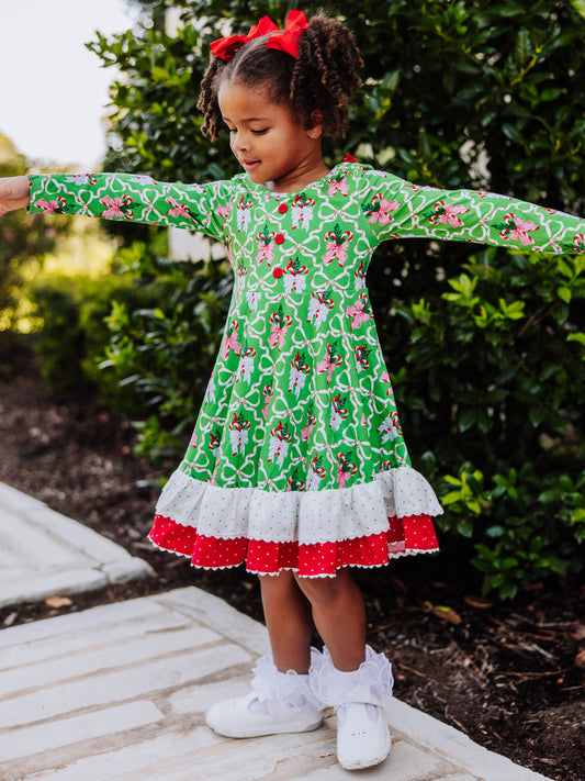 Girl is standing outside holding arms out. She is wearing a holiday themed dress with ruffly socks and white shoes. 