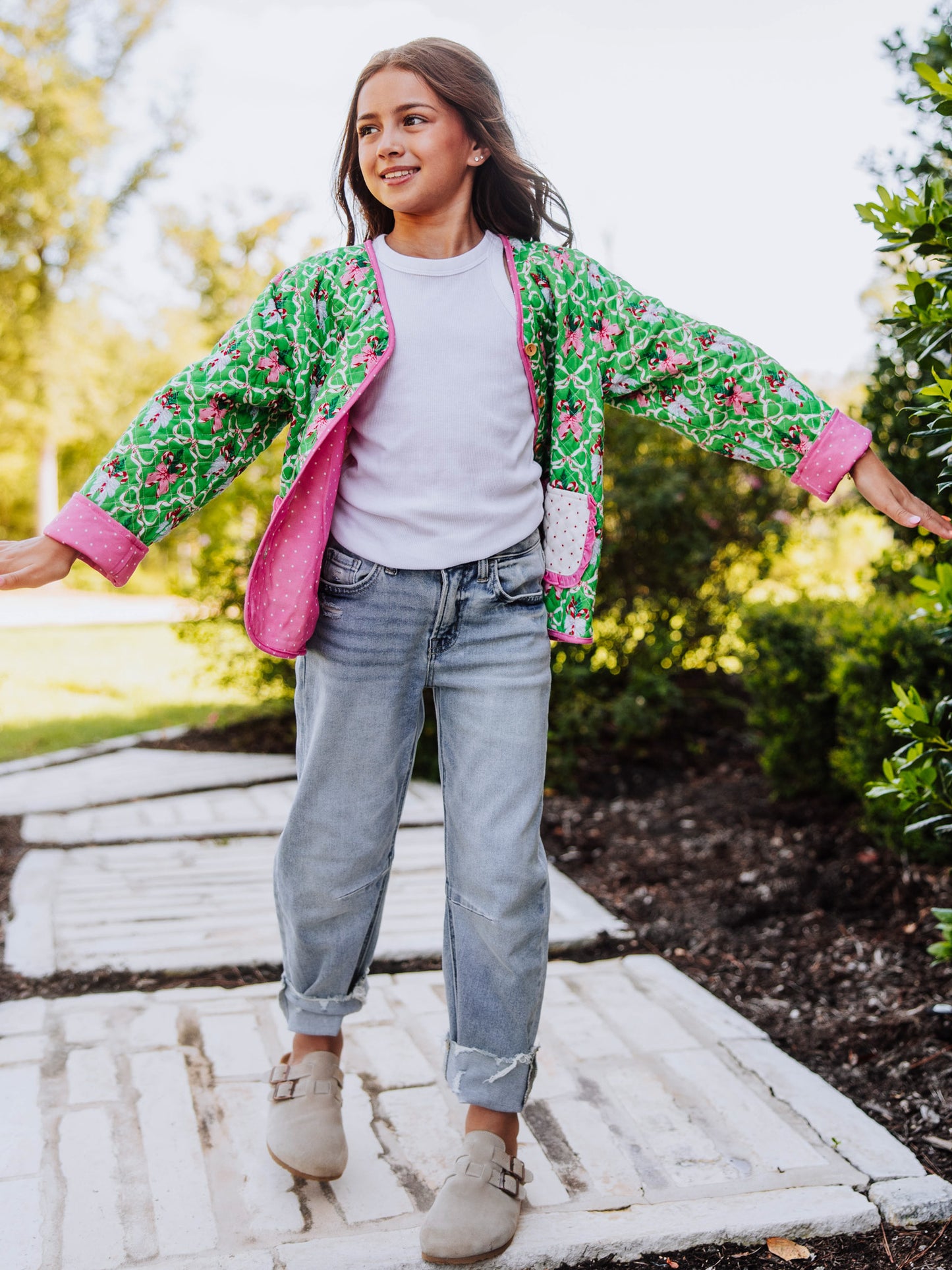 Girl holding arms out wearing a quilted holiday themed cardigan with jeans and our tan clogs