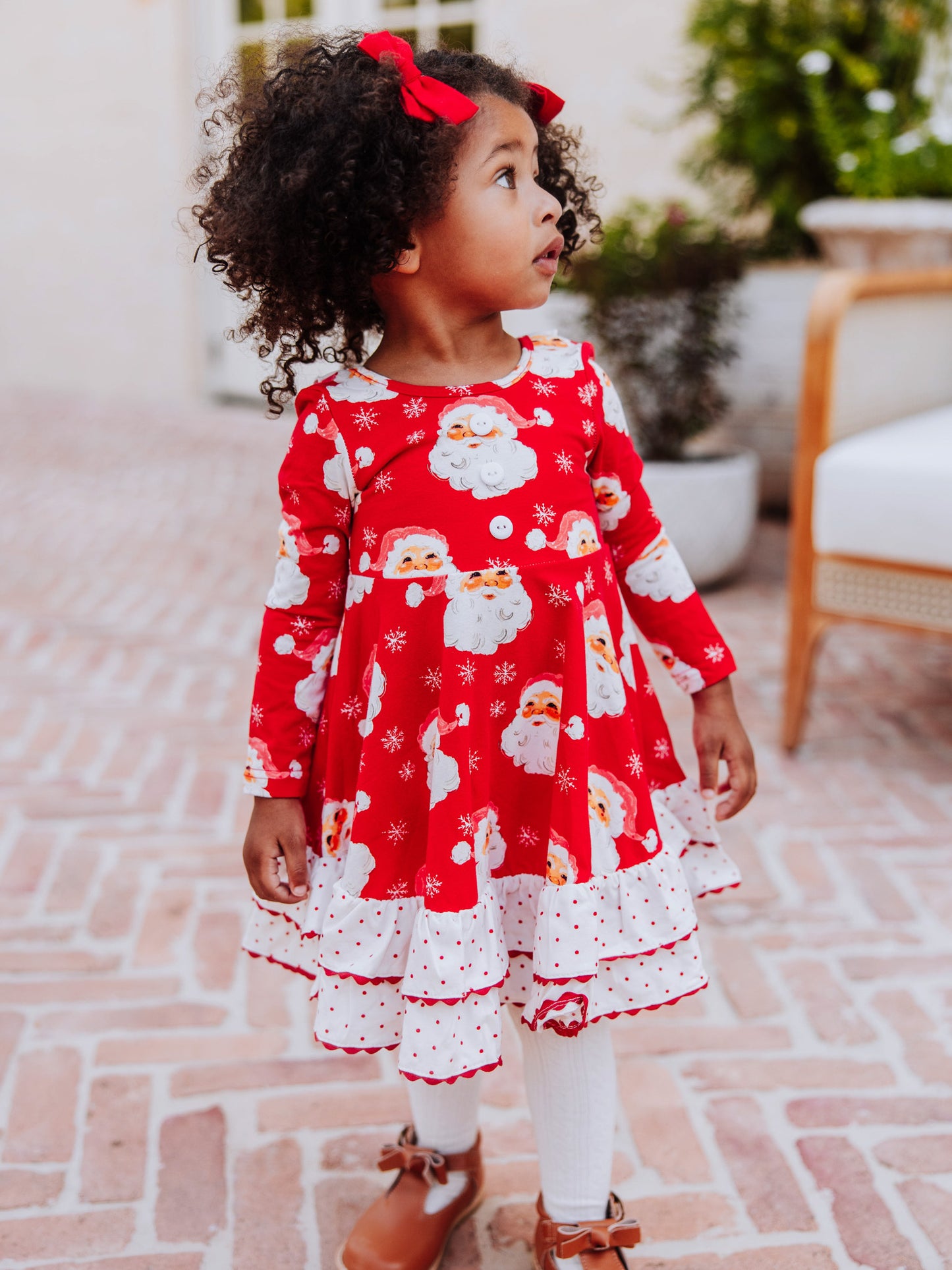 Girl standing outside wearing a red jolly santa dress with white tights and brown boots. 