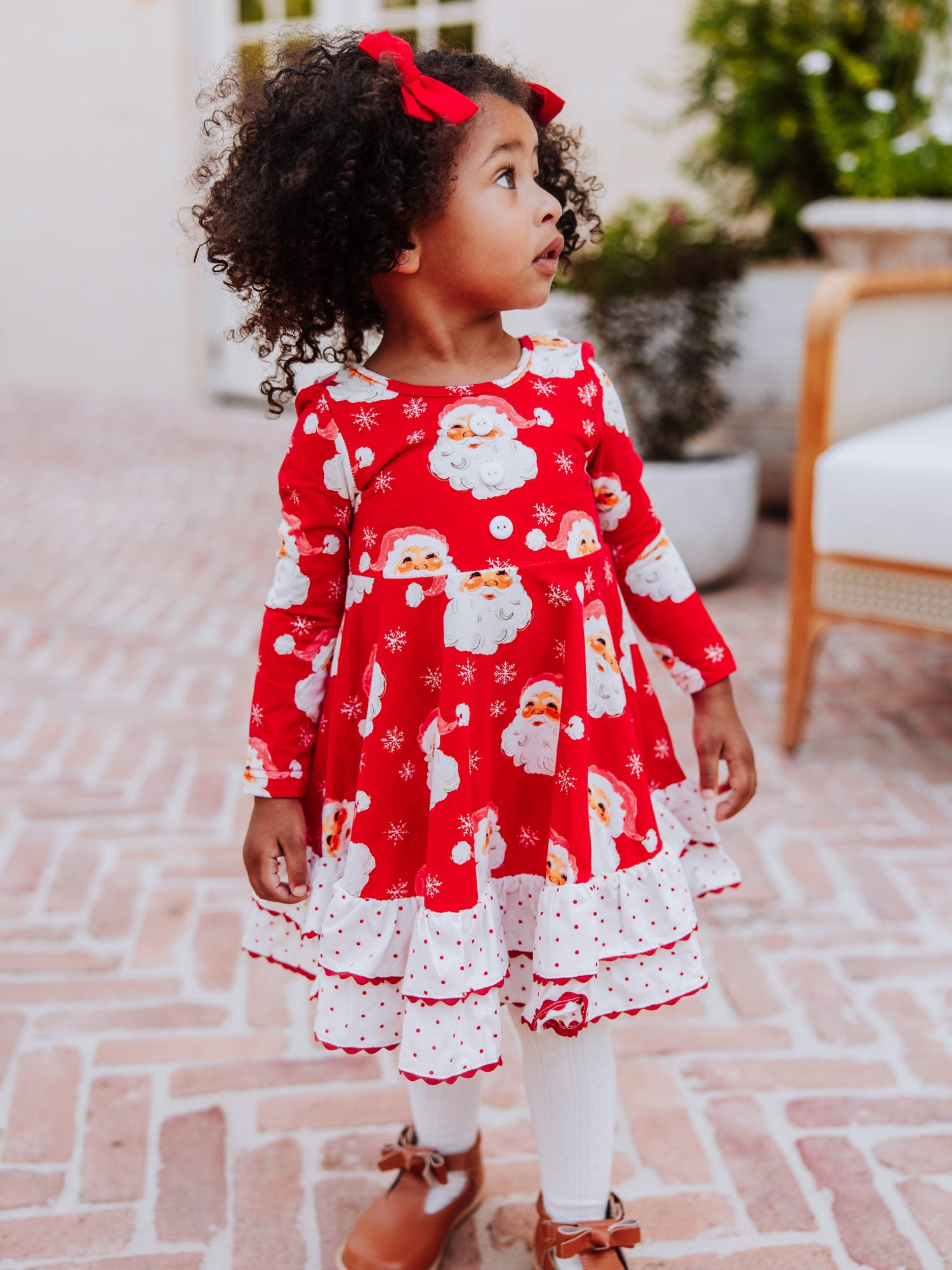 Girl standing outside wearing a red jolly santa dress with white tights and brown boots. 