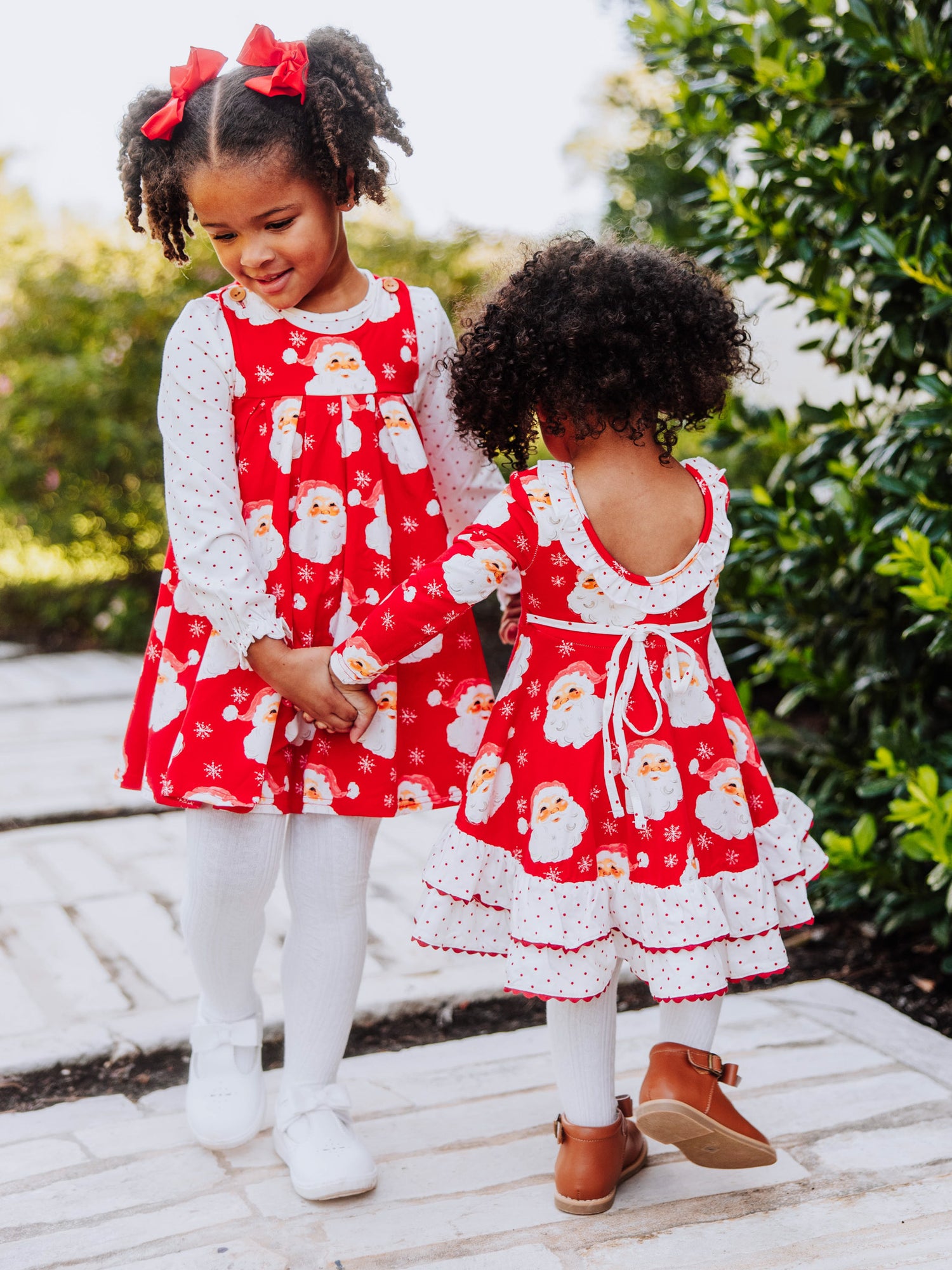 Two girls holding hands-both wearing same holiday printed garments; One girl is wearing a retro jumper and the other a vintage flair dress.