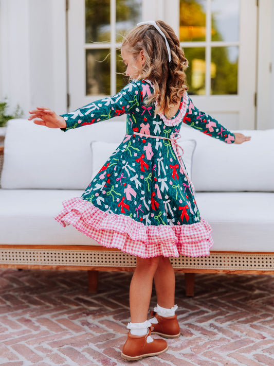 Girl standing in front of couch with arms out to side wearing a colorful holiday themed dress. 