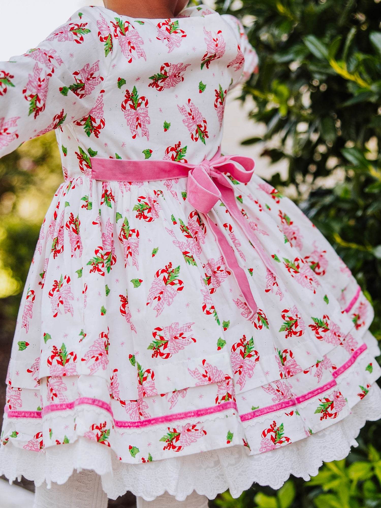 Picture shows the back of holiday themed dress with pink velvet tie at back. 