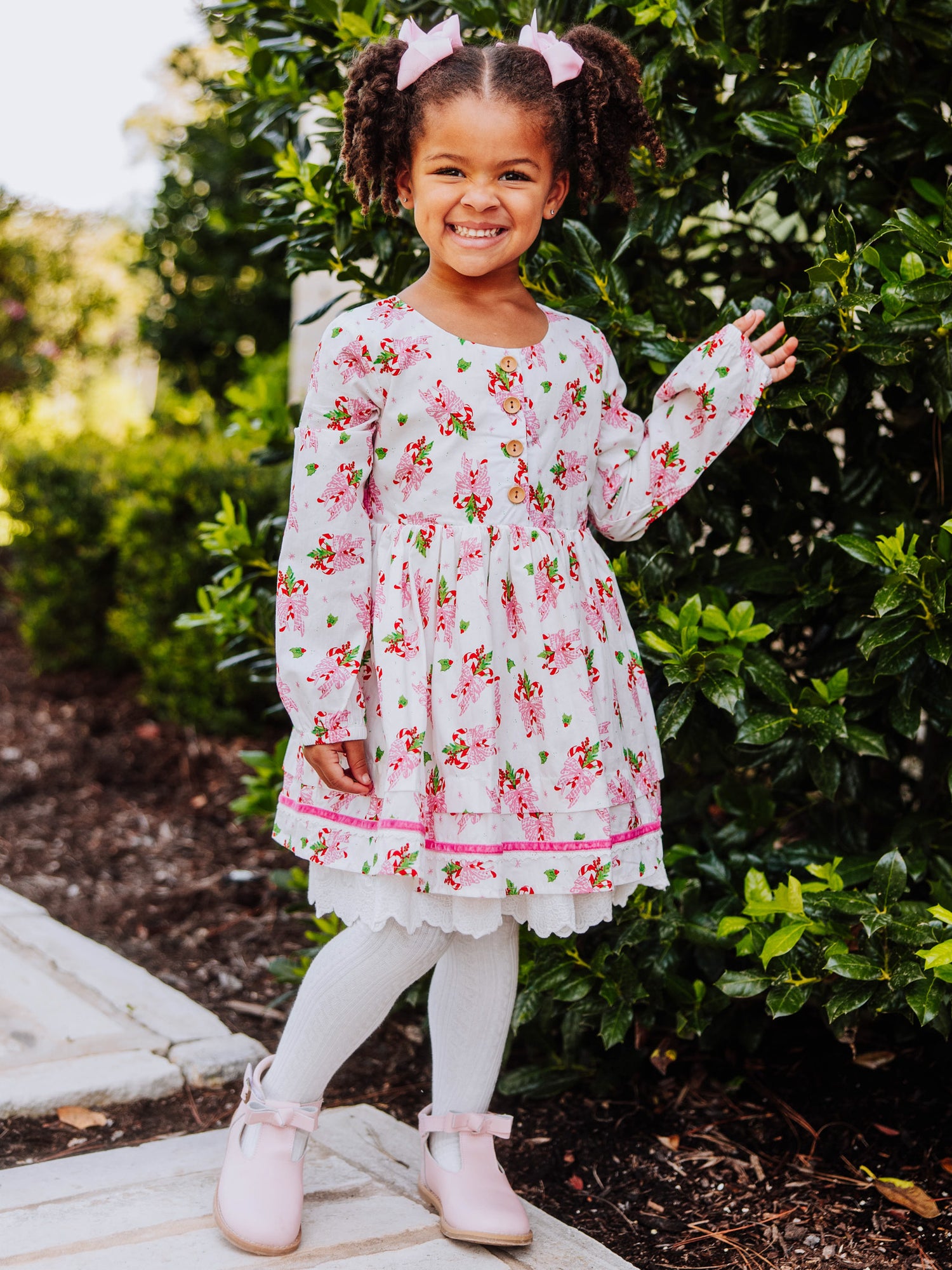 Girl standing outside next to greenery wearing a holiday themed dress. 