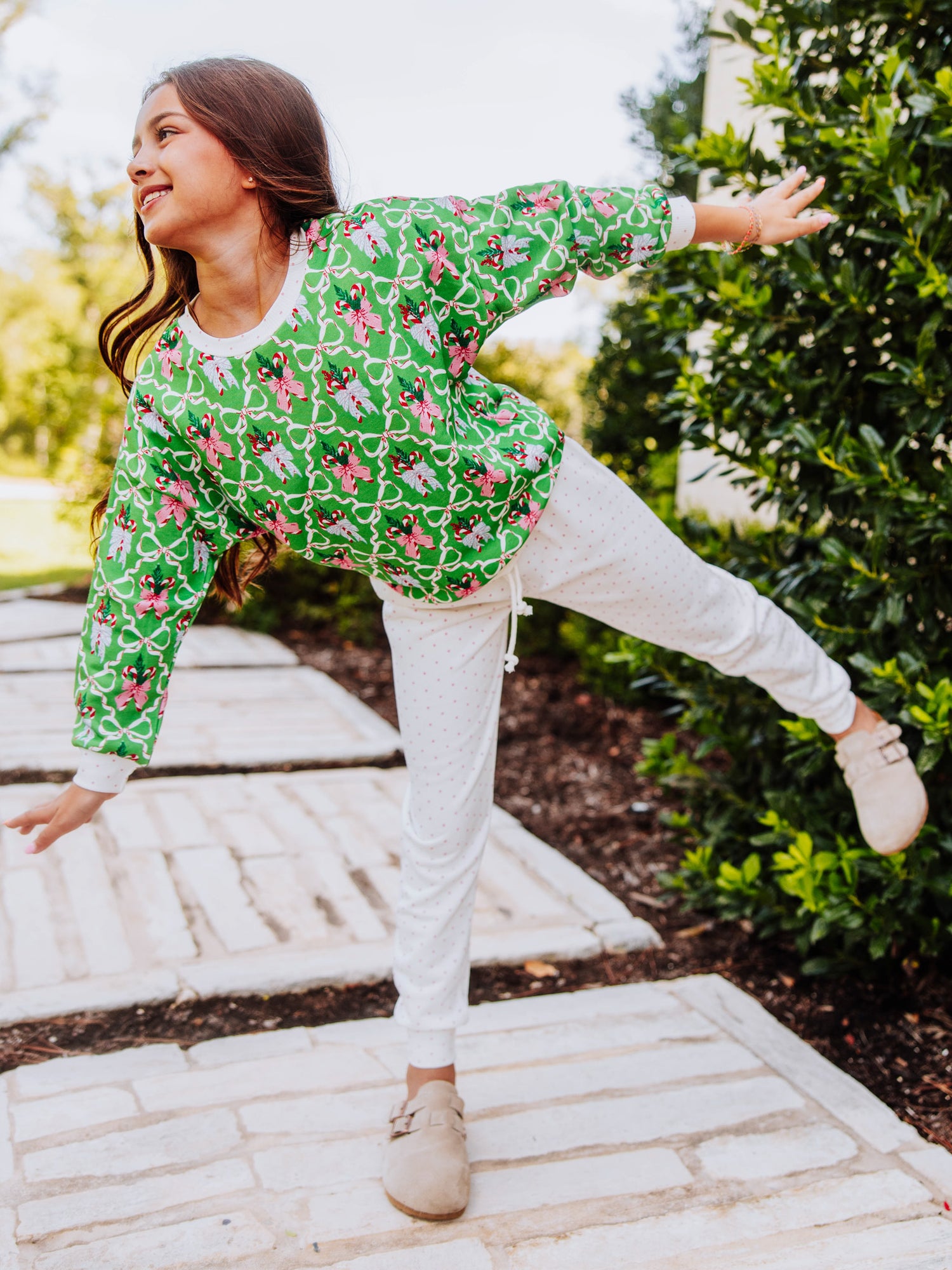 Girl standing outside with hands on hips wearing a holiday themed sweat set with tan clogs. 