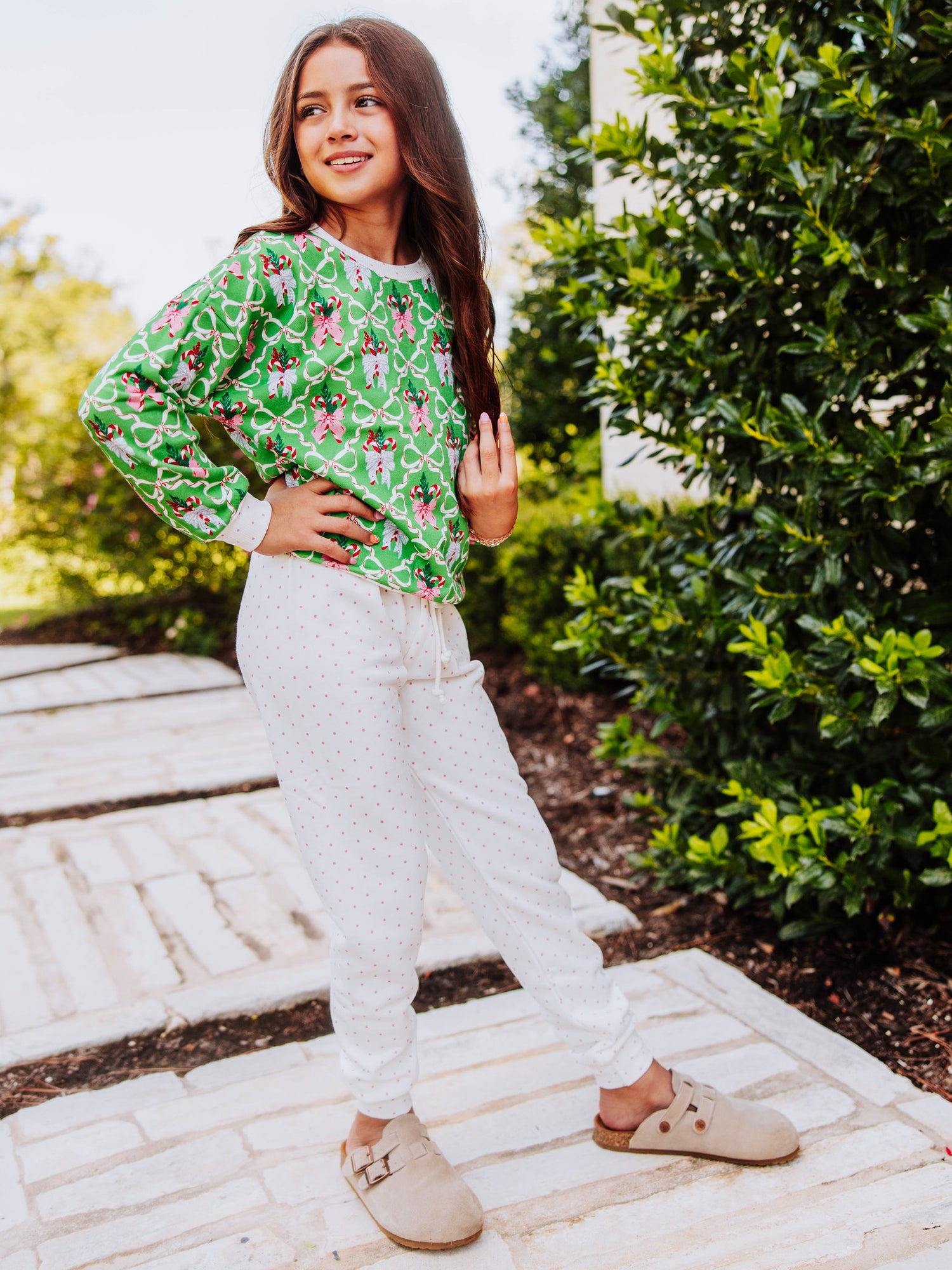 Girl standing outside with hands on hips wearing a holiday themed sweat set with tan clogs. 