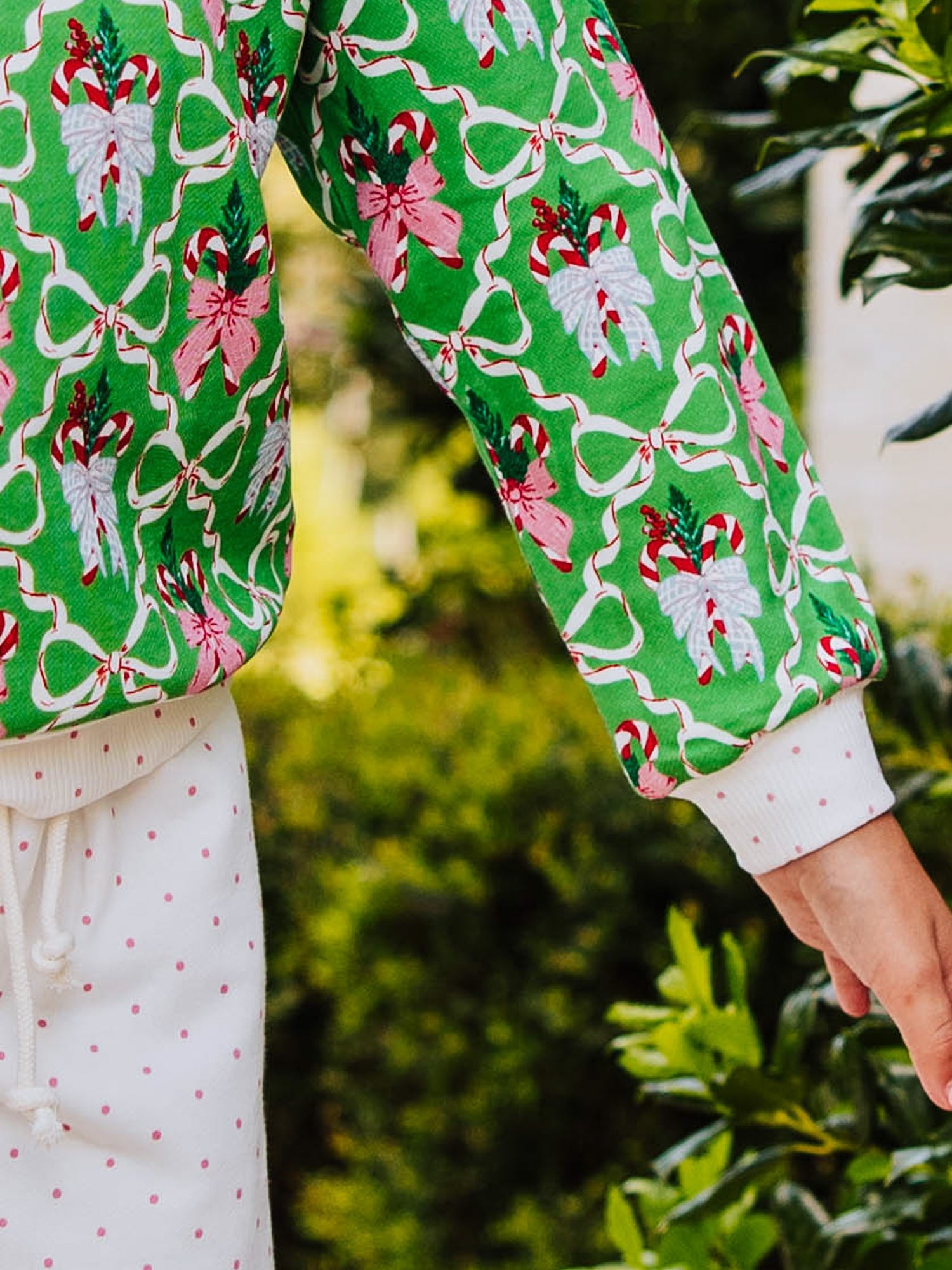 Up close of holiday print. Green with different colored ribbon bows with pink polka dots on hem, pants, and cuff