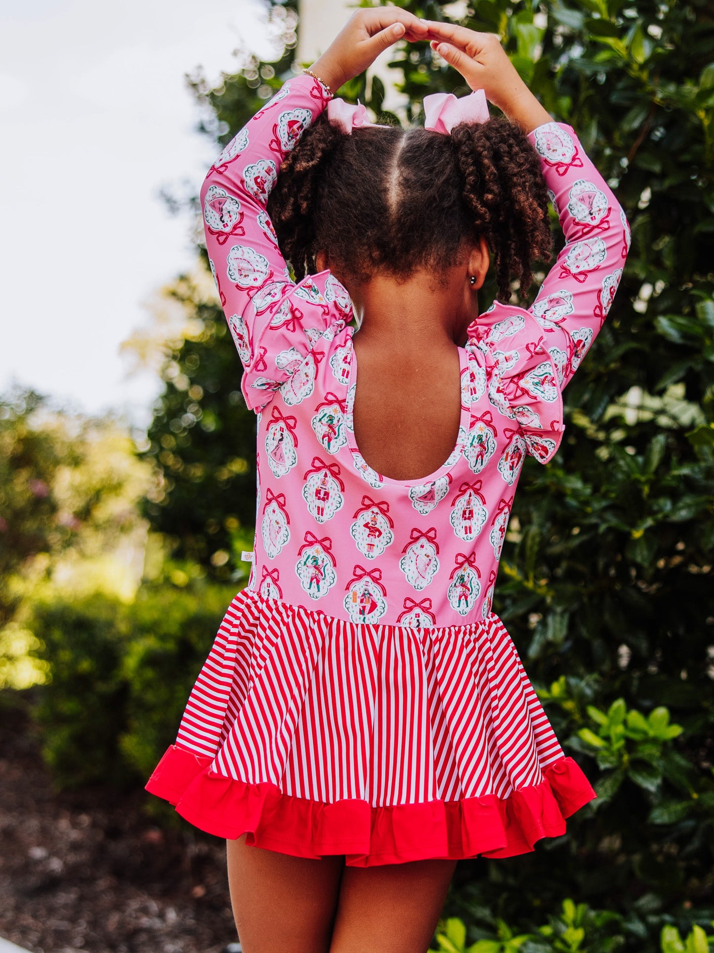 Model is wearing a holiday themed skirted leotard with her hands up above her head in a traditional ballet stance. 