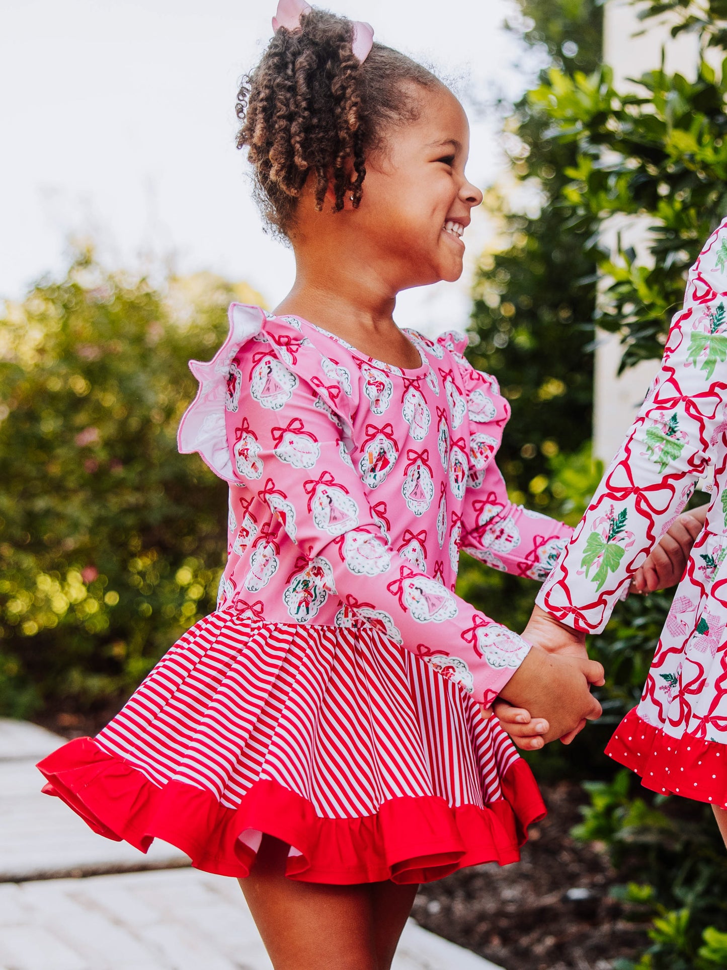 Model is holding hands with someone and is smiling. Model is wearing a holiday themed skirted leotard. 