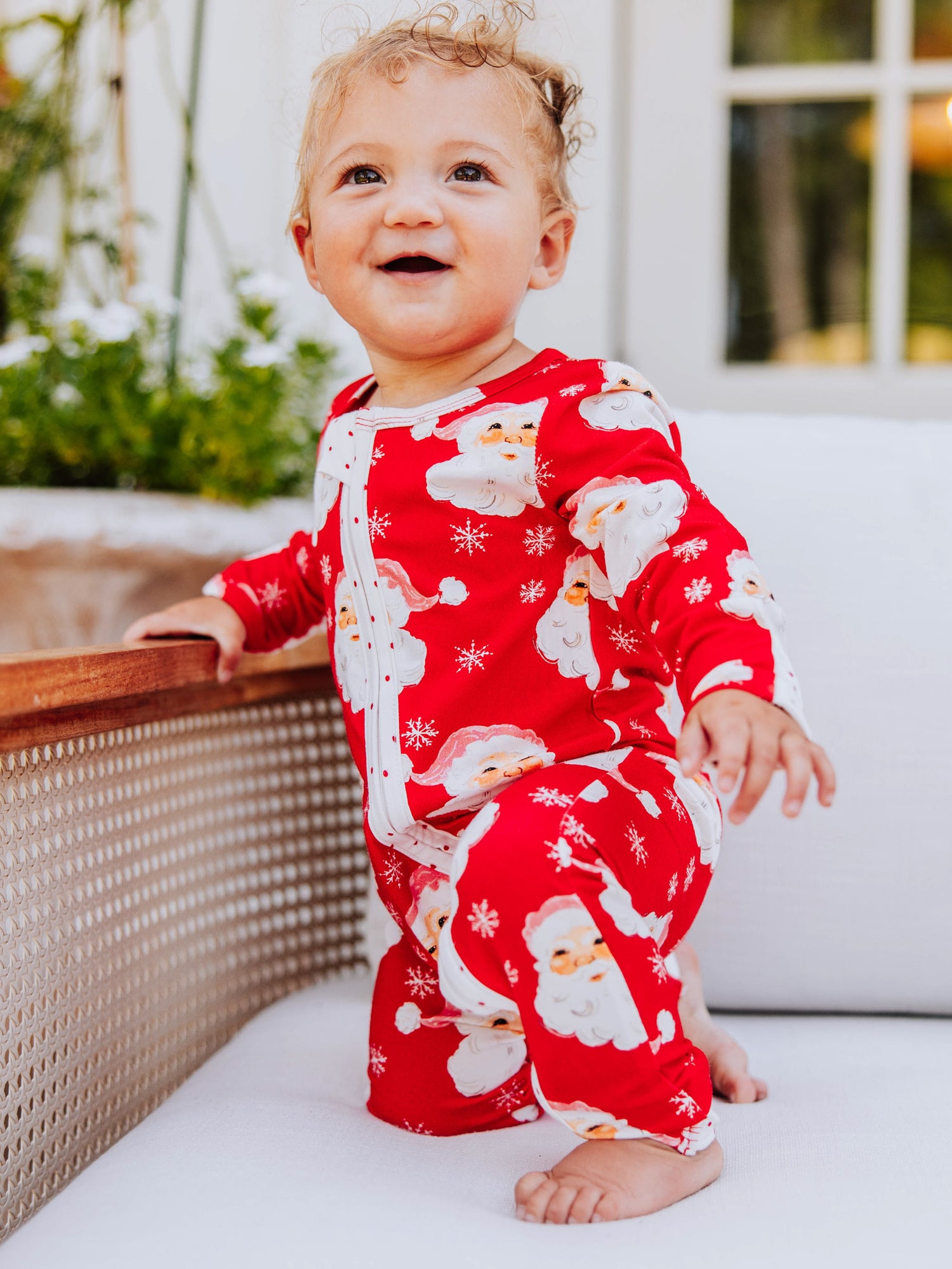 baby girl wearing a red Santa layette on a couch.