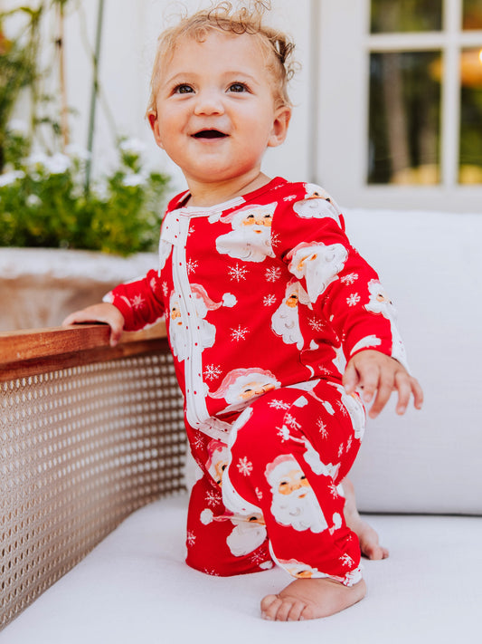 baby girl wearing a red Santa layette on a couch.