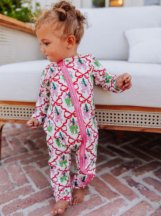 Baby standing up holding on to white couch smiling. Baby is wearing a colorful printed layette. 