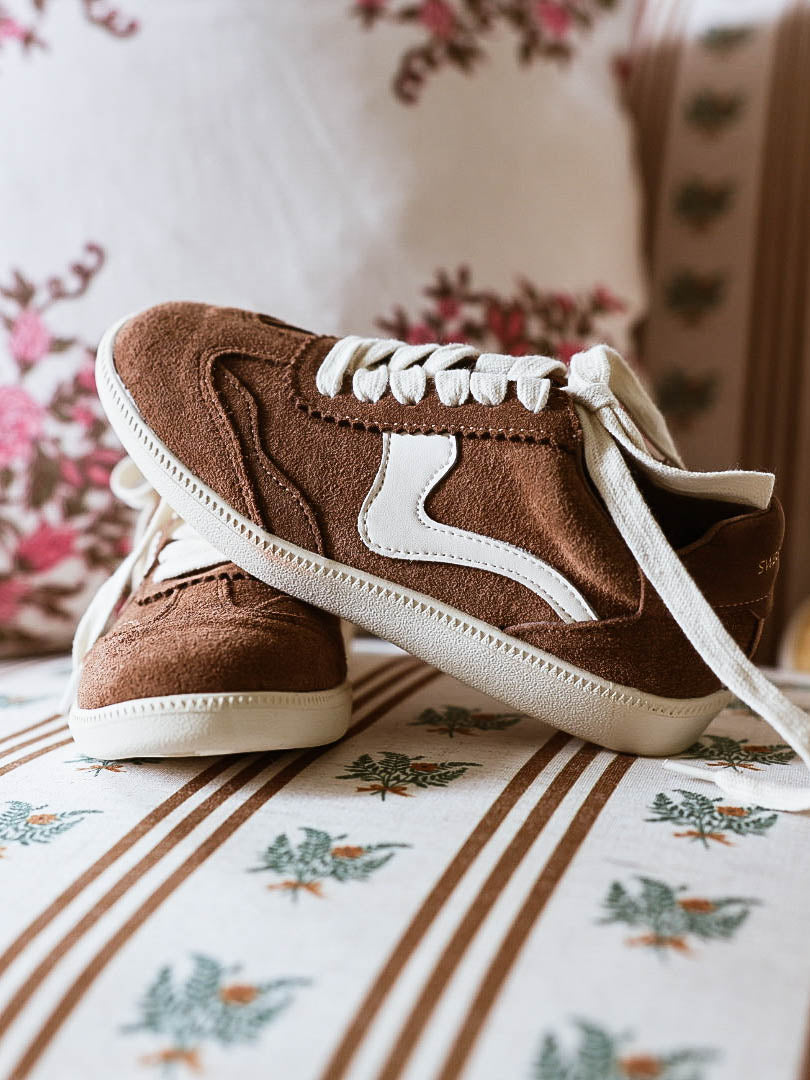 Brown mocha colored suede sneakers with a swish design on the side in a creamy white and creamy white laces.