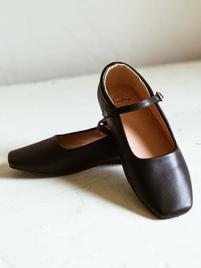 Picture of black ballet mary janes with square toe and a clasp buckle closure. White background