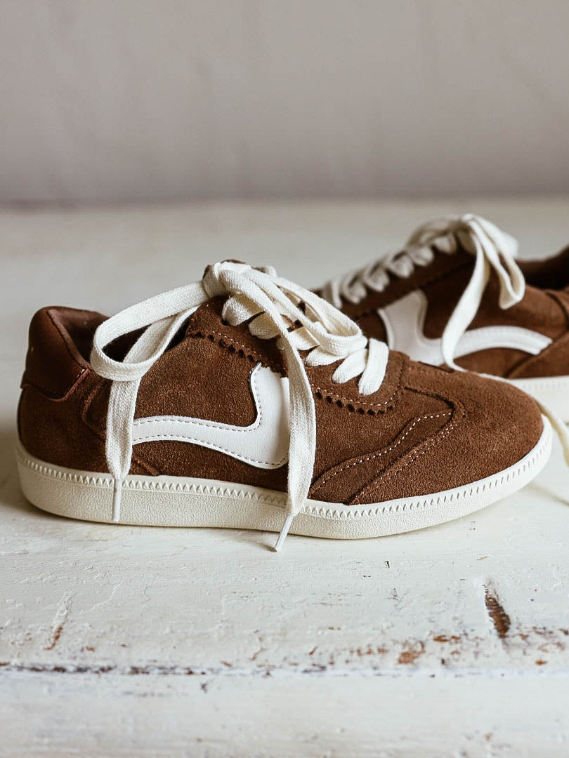 Brown mocha colored suede sneakers with a swish design on the side in a creamy white and creamy white laces.