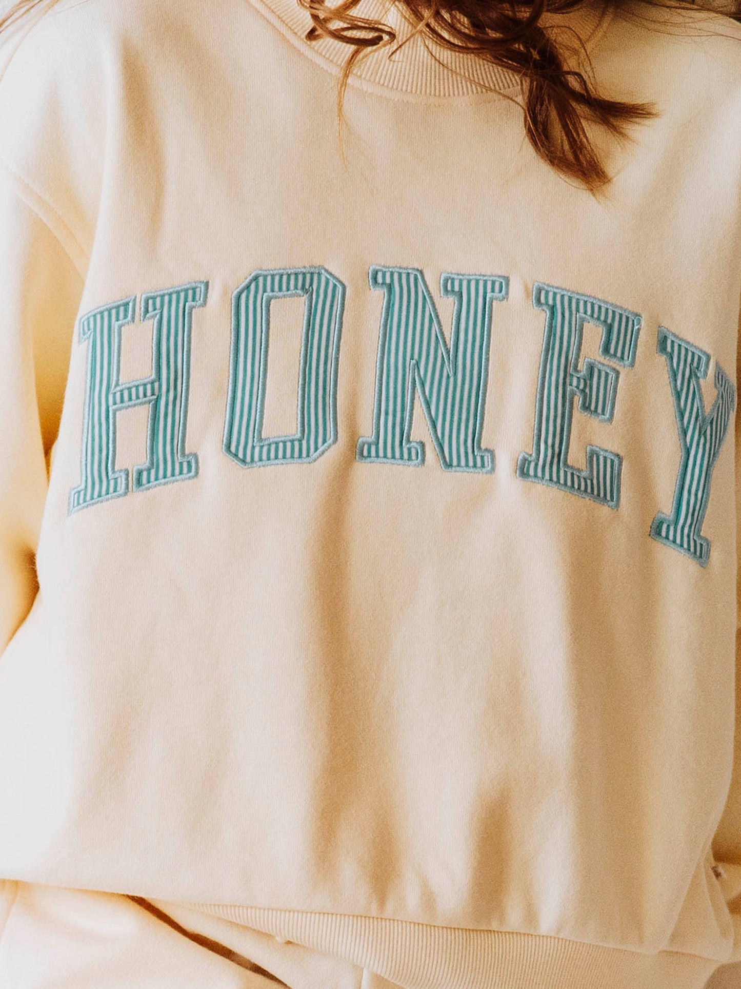 Model wearing a yellow, two-piece mock neck set. The top has HONEY on the front with blue pin stripes. Bottoms are the same color as the top. 