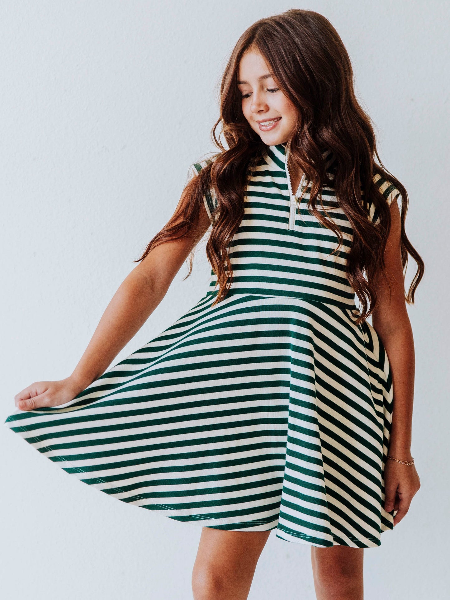 Model wearing a green and ivory striped dress. Dress has a zipper closure at chest. Model is holding the corner of the dress. 