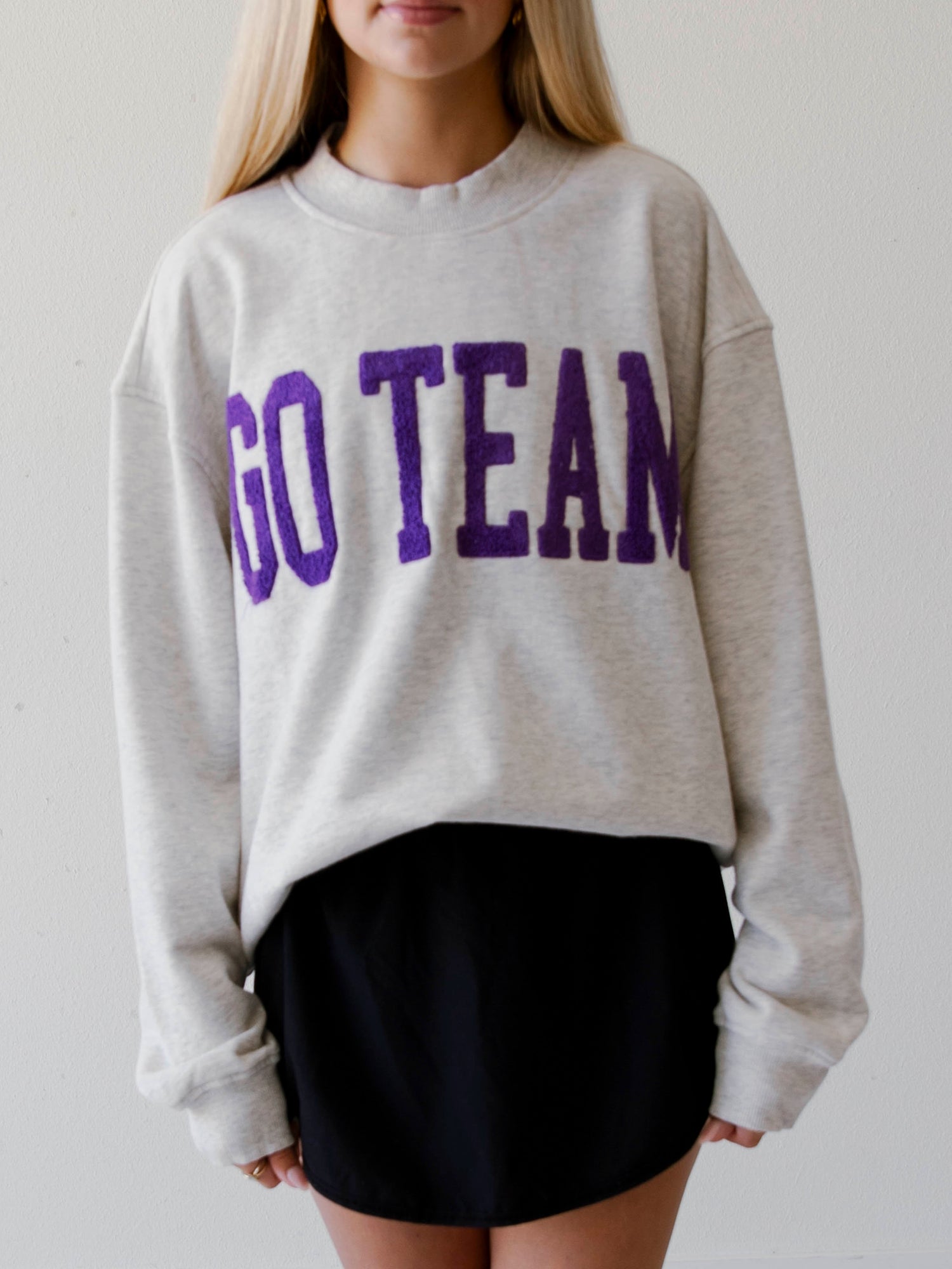 Girl wearing a heathered gray sweater that says GO TEAM in purple.
