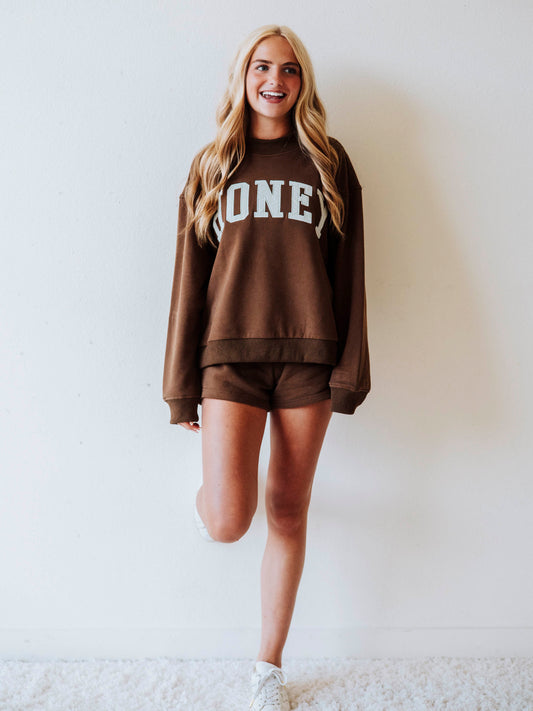 Girl wearing a chocolate brown mock neck sweatshirt  set that says HONEY on the front. Bottoms are the same chocolate brown as top.