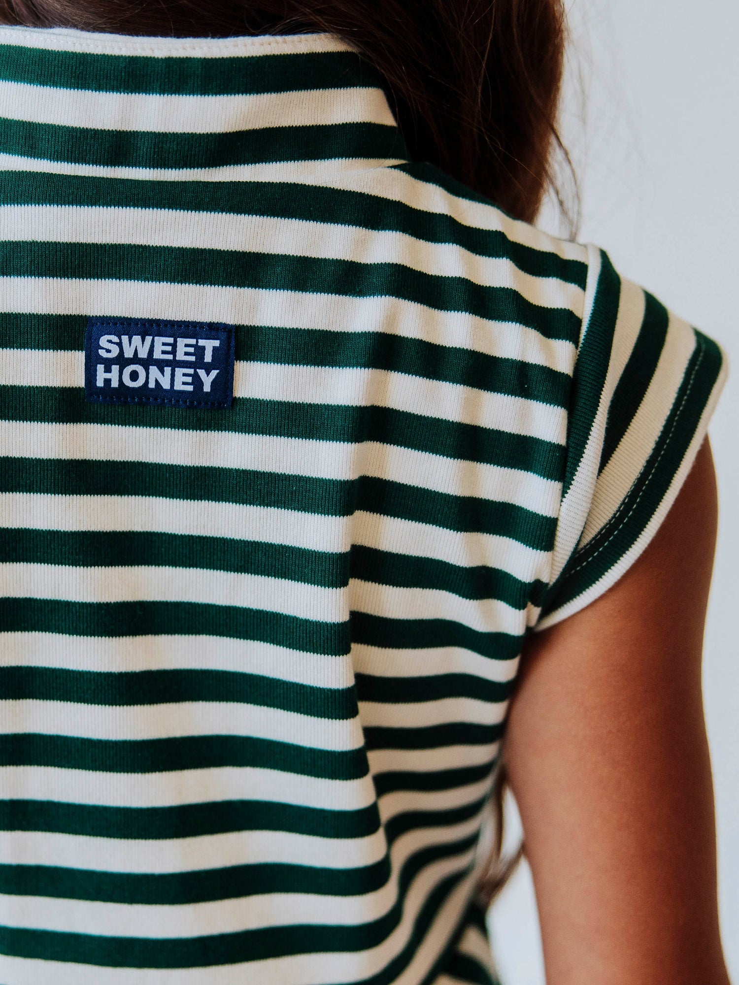 Close up of stitched, sweethoney tag at back that is navy and white in color. Dress model is wearing is green and ivory. 