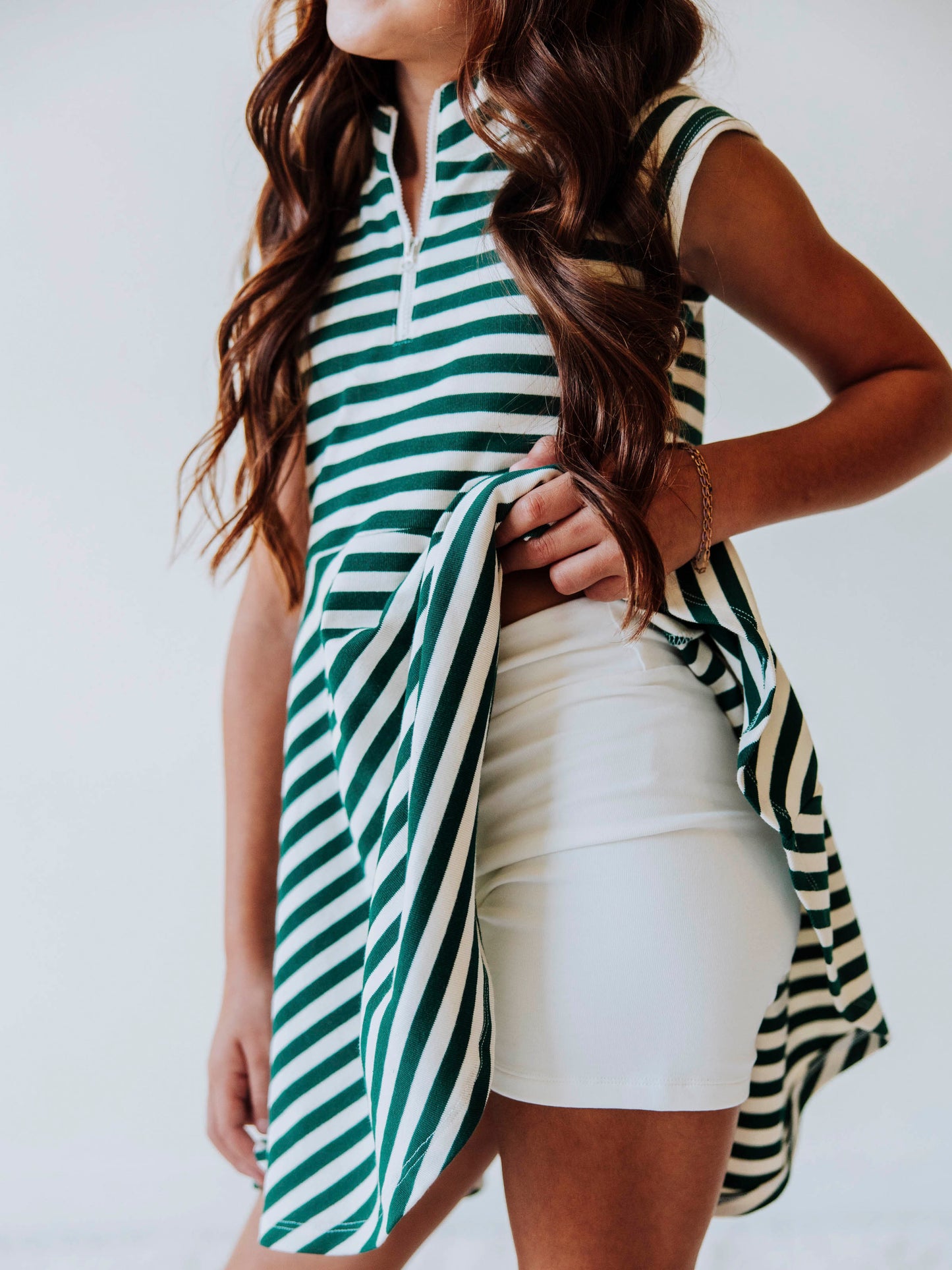 Model wearing a green and ivory striped dress with zipper closure at chest. Model is lifting up side of dress to show ivory gym shorts underneath. 