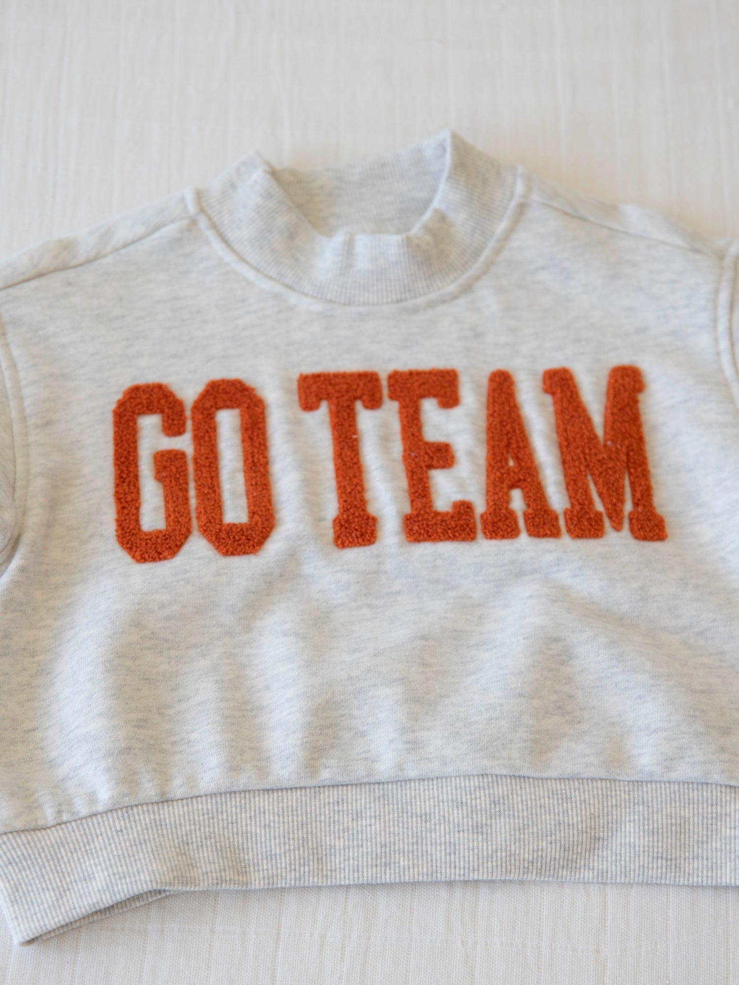 Flat lay of heathered gray sweatshirt that says GO TEAM in burnt orange. 