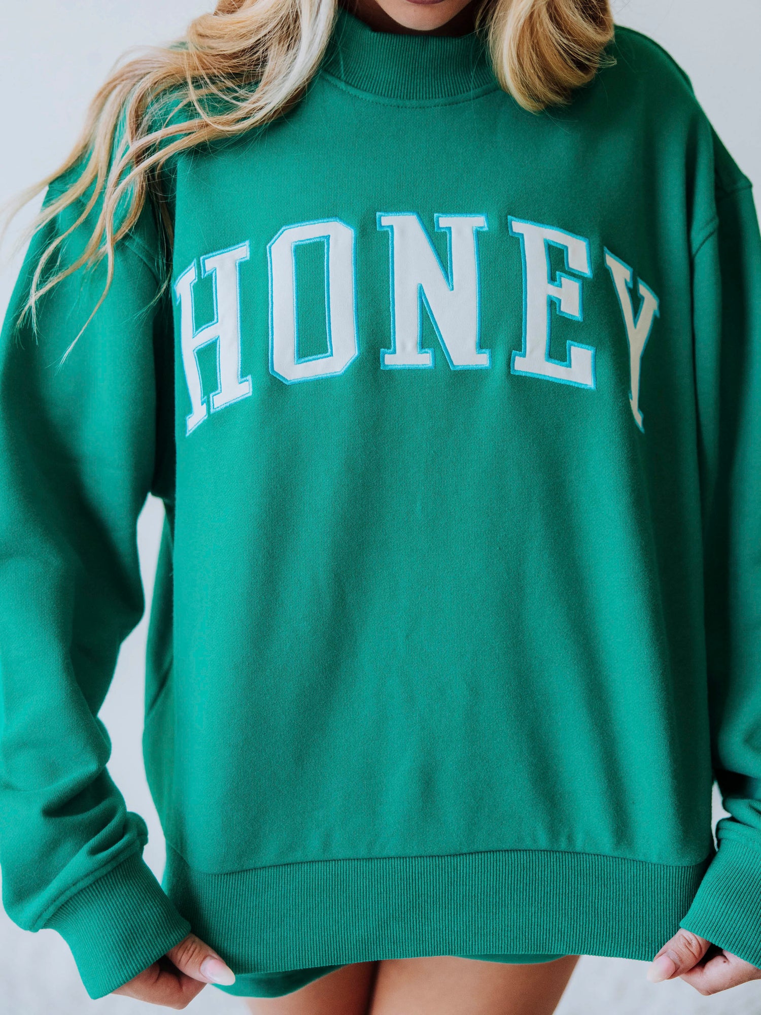 Girl wearing a teal two piece set. Top says HONEY on the front. Shorts are same teal color as top. This picture is a close-up of HONEY top