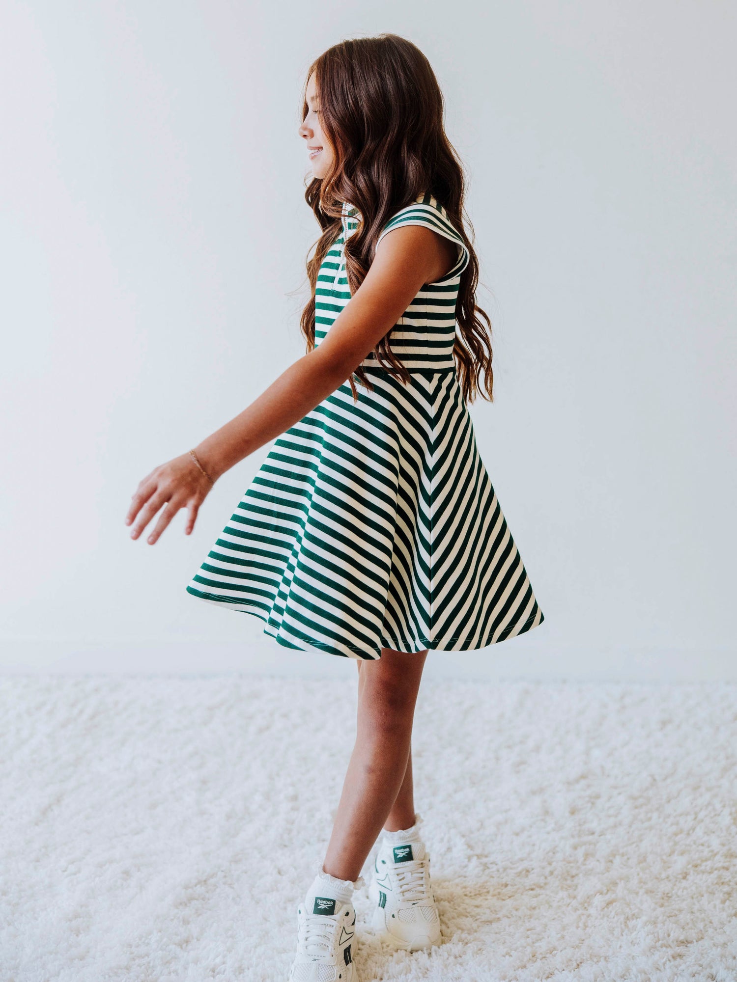 Model is wearing a green and ivory striped dress and is twirling. 