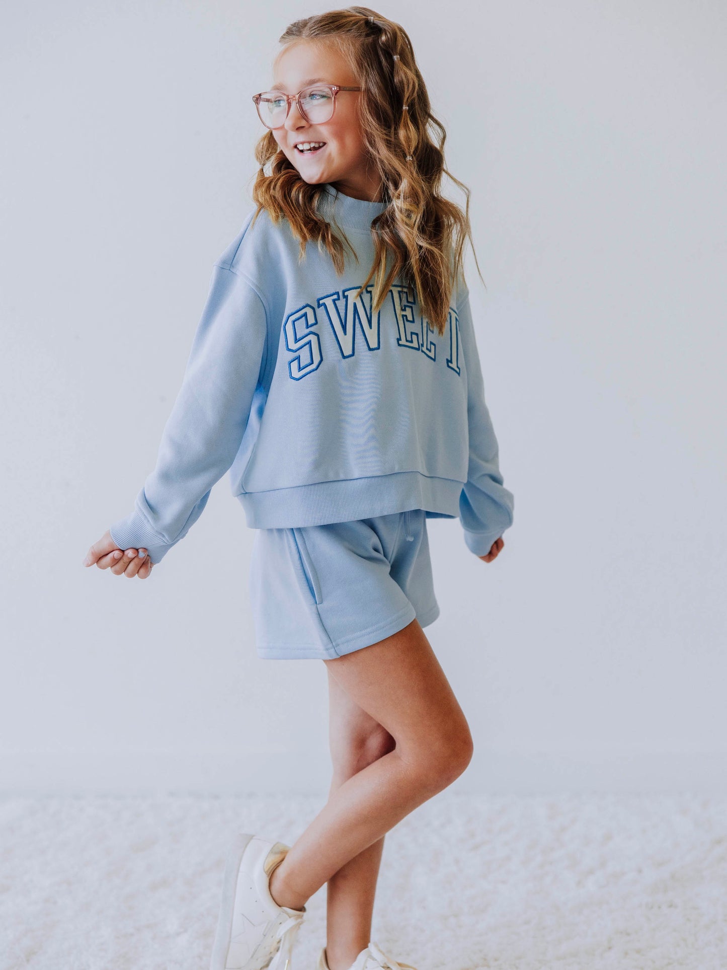 Model wearing a light blue two piece jogging set. Top says SWEET and the bottoms are the same color blue as top. 