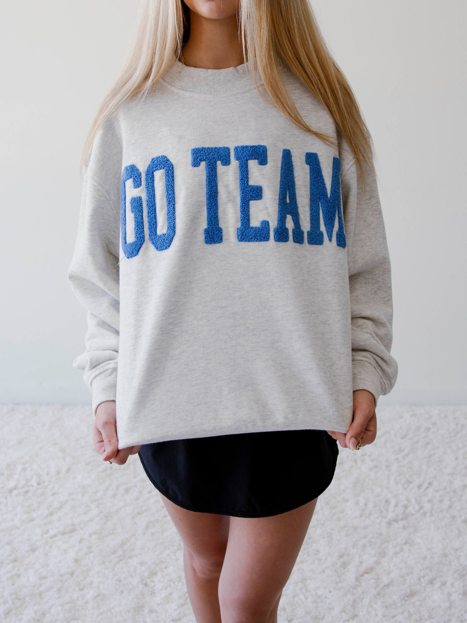 Girl wearing a sweater that says go team in royal blue.