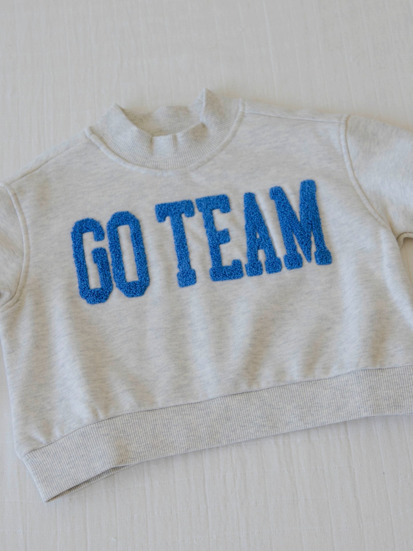 flay lay of a heathered gray sweater that says go team in royal blue
