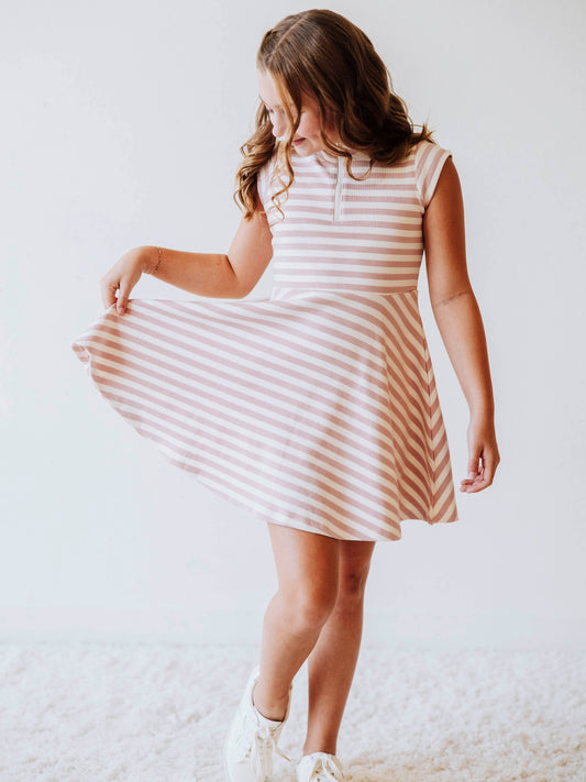 Model wearing a pink and ivory striped dress. Model is holding the corner of dress out. 