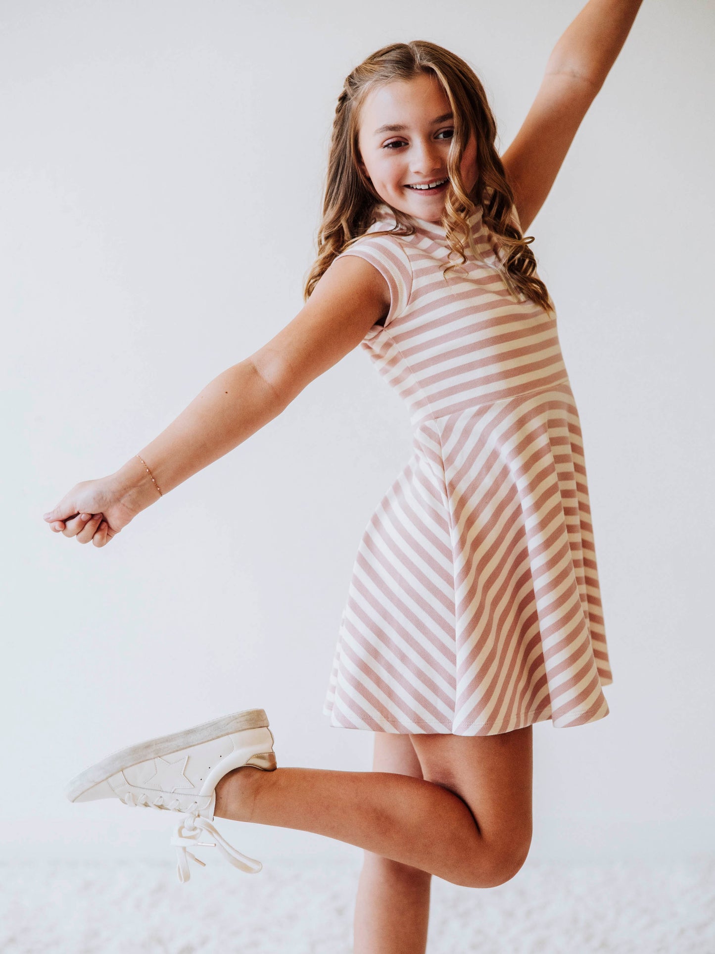 Model is posing wearing a pink and ivory striped dress with white shoes. 