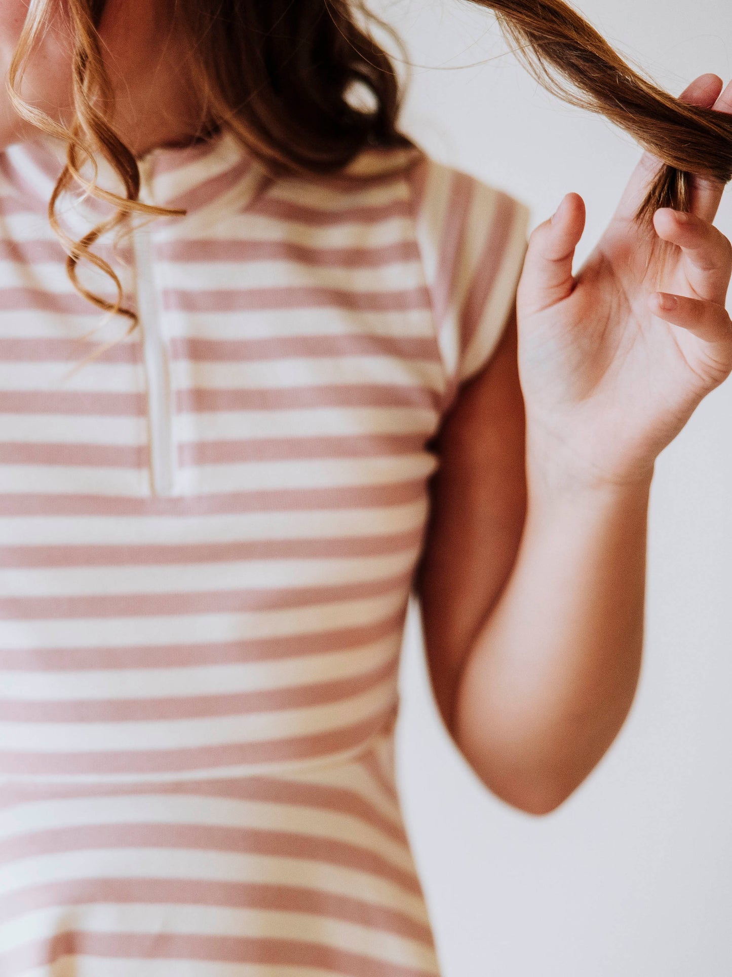 Close up of pink and ivory striped dress zipper closure at chest. Model is twirling hair. 