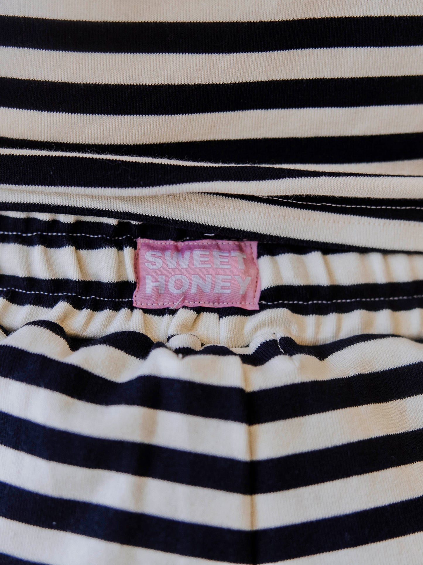 Close up of Sweehoney stitched logo tag on the back of ivory and navy stiped pants waistband