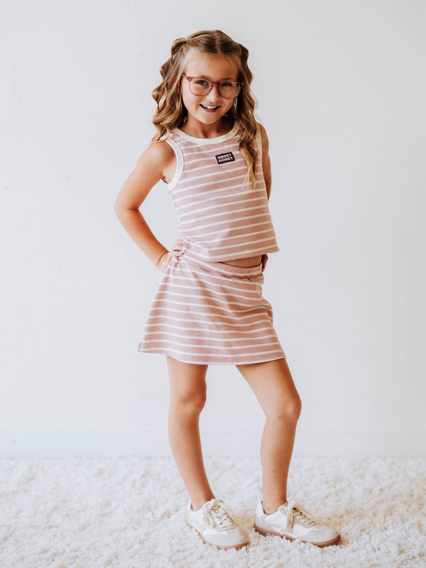 Model is wearing a pink and ivory striped two piece skort set. There is a sweethoney stitched tag on the middle of chest of shirt. 